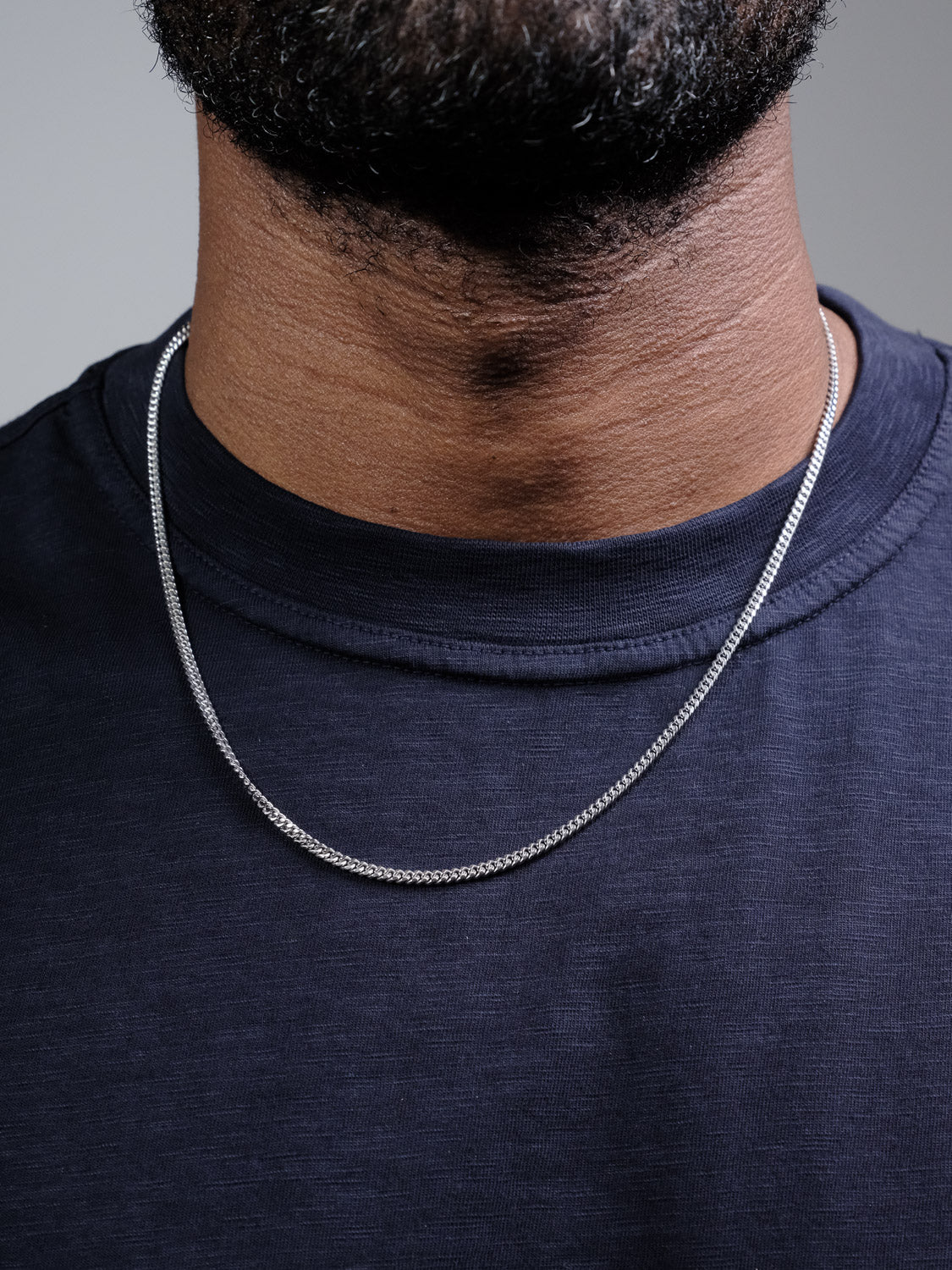 Close-up of a person wearing the Blaze 100 Miami Cuban Necklace by ID Menswear with a dark navy shirt, showing only the lower face and neck.