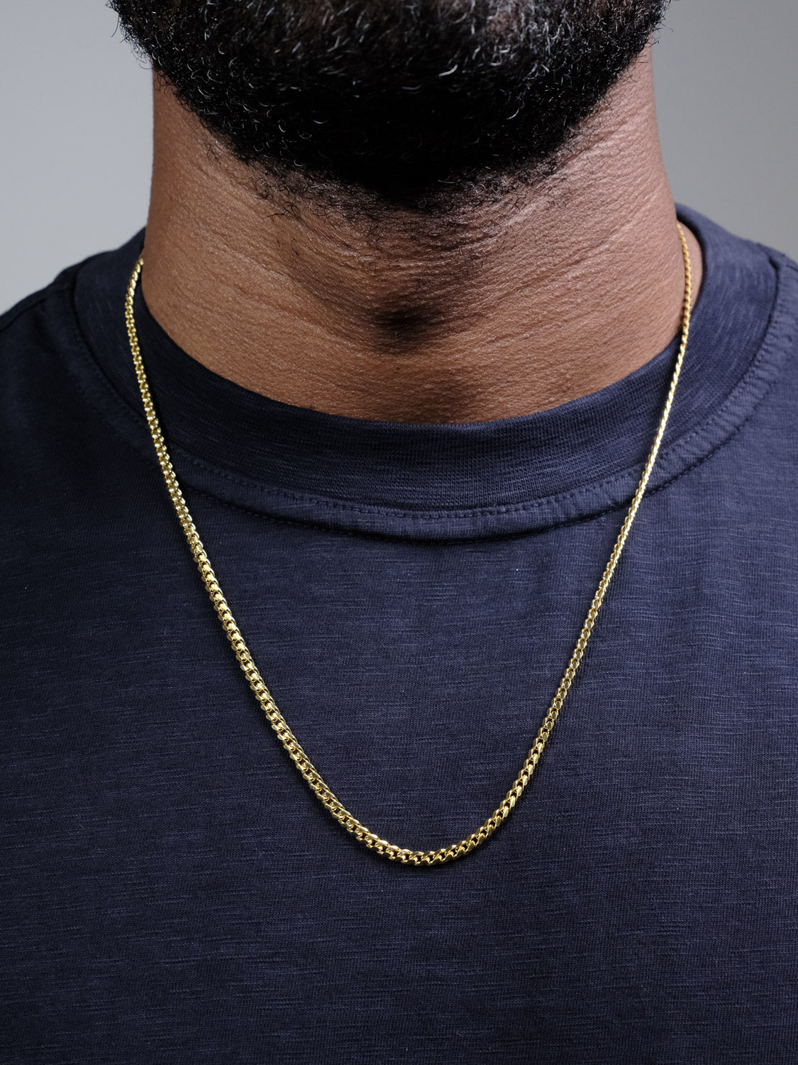 A close-up of a person wearing the Blaze 80 Miami Cuban Necklace by ID Menswear over a dark navy blue crew neck shirt, with only the lower half of their face and neck visible.