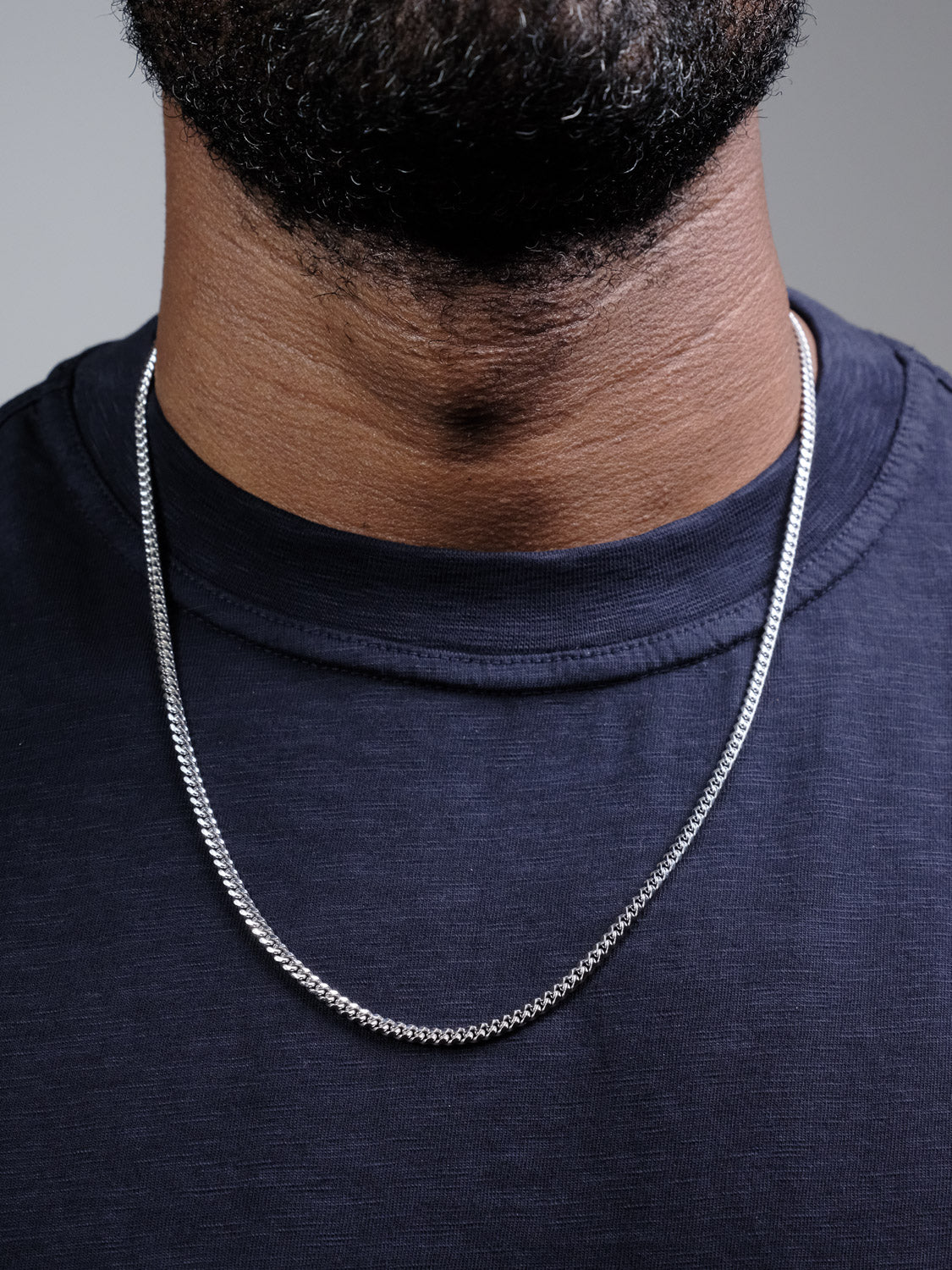 A close-up of a person wearing a dark navy t-shirt and the Blaze 80 Miami Cuban Necklace by ID Menswear in 925 Sterling Silver, showing only the lower face, neck, and upper chest.