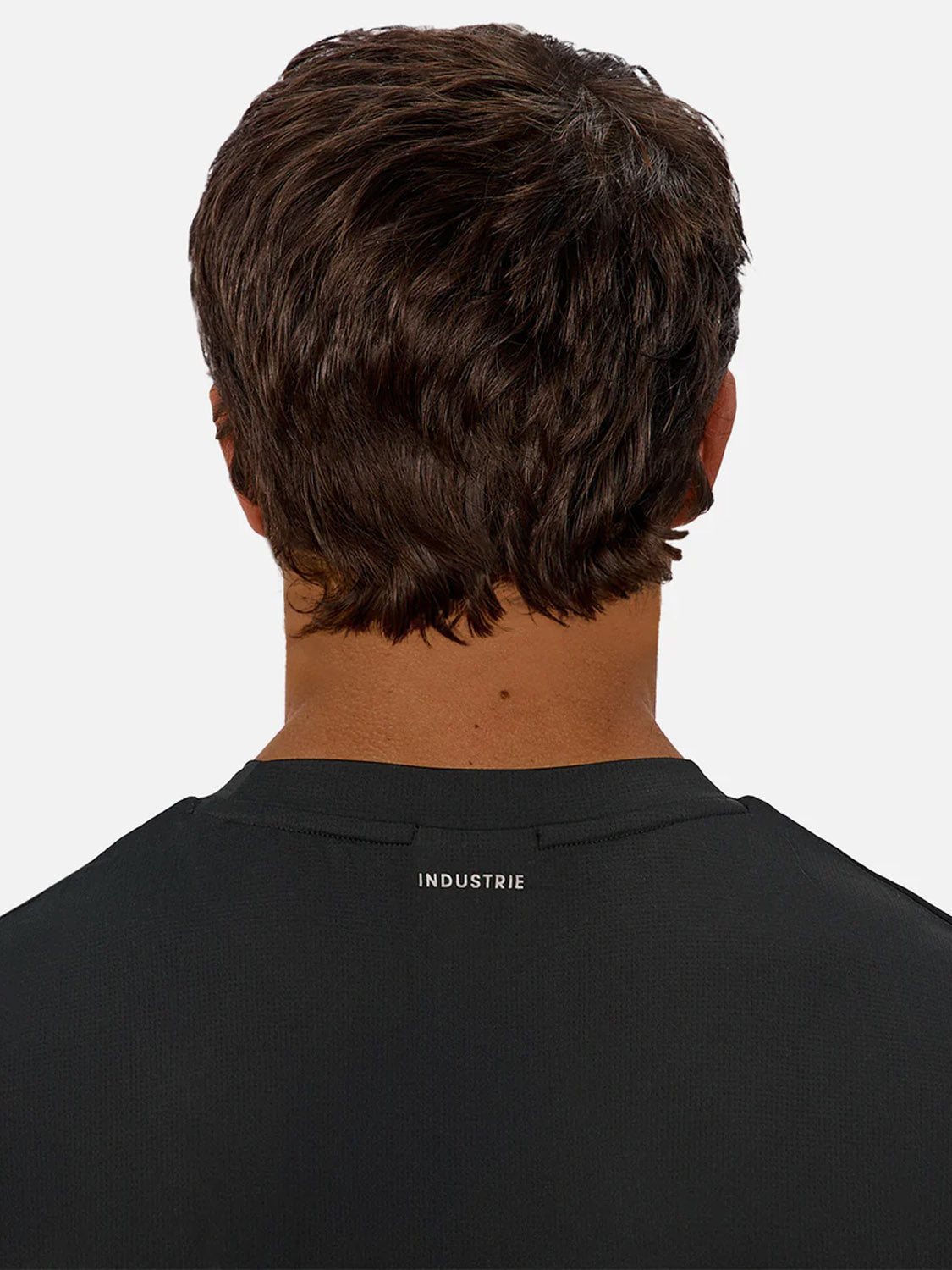 A man with short brown hair is seen from behind wearing the Industrie Boldon T-Shirt, a black, lightweight athletic tee featuring "INDUSTRIE" in white on the upper back, set against a plain white background.