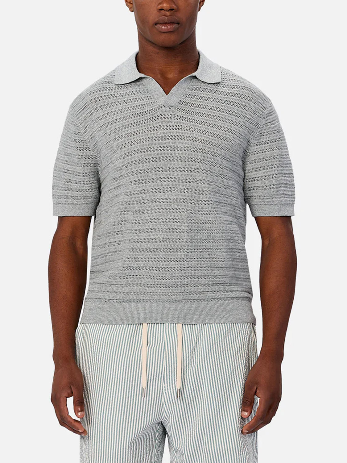 A man wearing Industrie’s The Bologna Polo in light gray and light gray and white striped drawstring shorts stands against a plain white background.