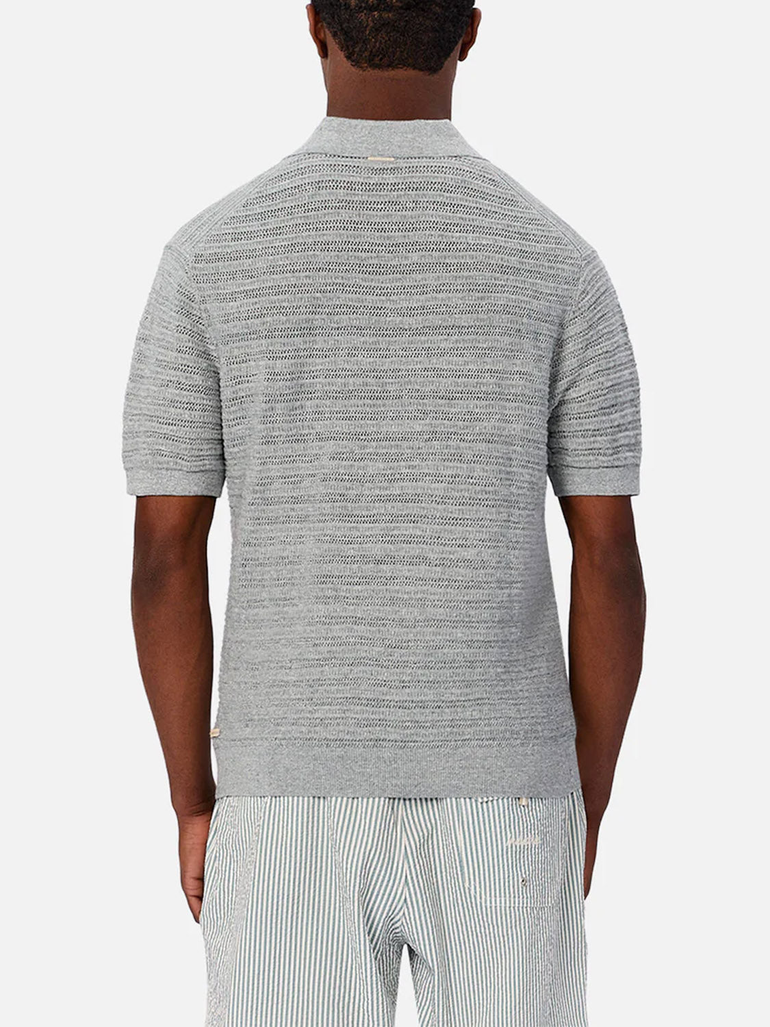 A man faces away, wearing Industrie’s The Bologna Polo in light gray short sleeves with a spread collar and matching light gray and white striped shorts against a plain white background.