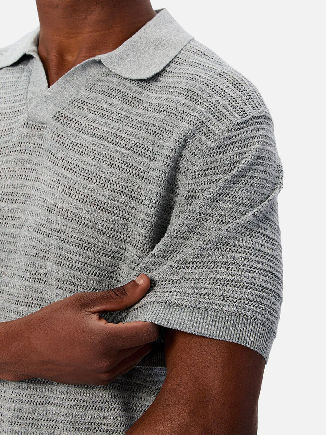 A person wearing The Bologna Polo by Industrie in light gray with short sleeves and a spread collar holds the sleeve with one hand against a plain white background.