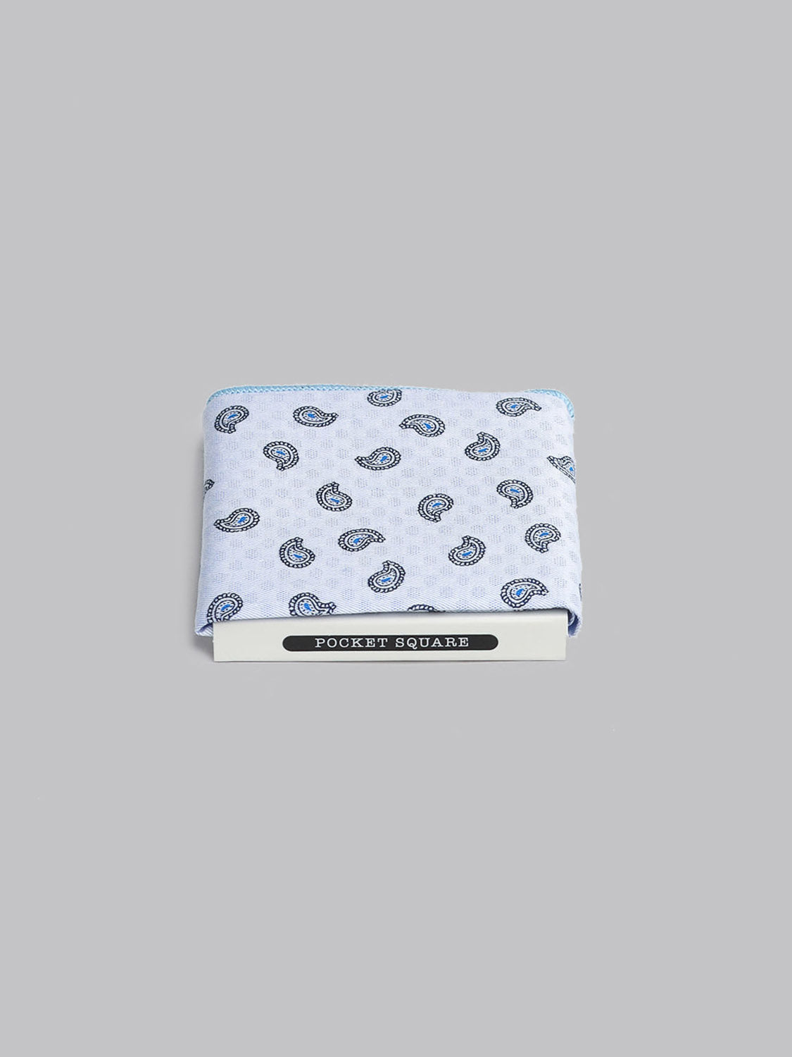 A folded light blue Bombay Pocket Square by ID Menswear, featuring a blue and black paisley pattern, handmade in Brooklyn from 100% cotton, is displayed against a gray background with the label POCKET SQUARE below.