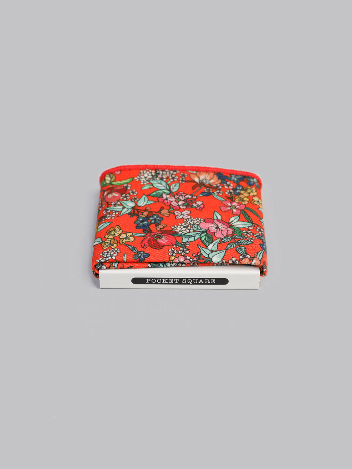 A Bouquet Pocket Square by ID Menswear, handmade in Brooklyn from 100% cotton with a red floral pattern, is neatly folded in white packaging labeled Pocket Square against a plain gray background.