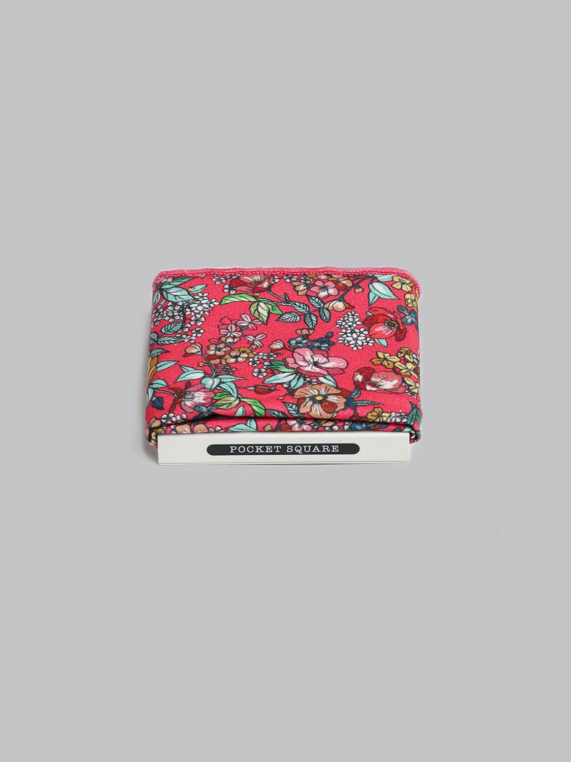 A folded red Bouquet Pocket Square by ID Menswear, handmade in Brooklyn from 100% cotton with a vibrant floral pattern, is shown on a light gray background. A Pocket Square label is attached at the bottom.