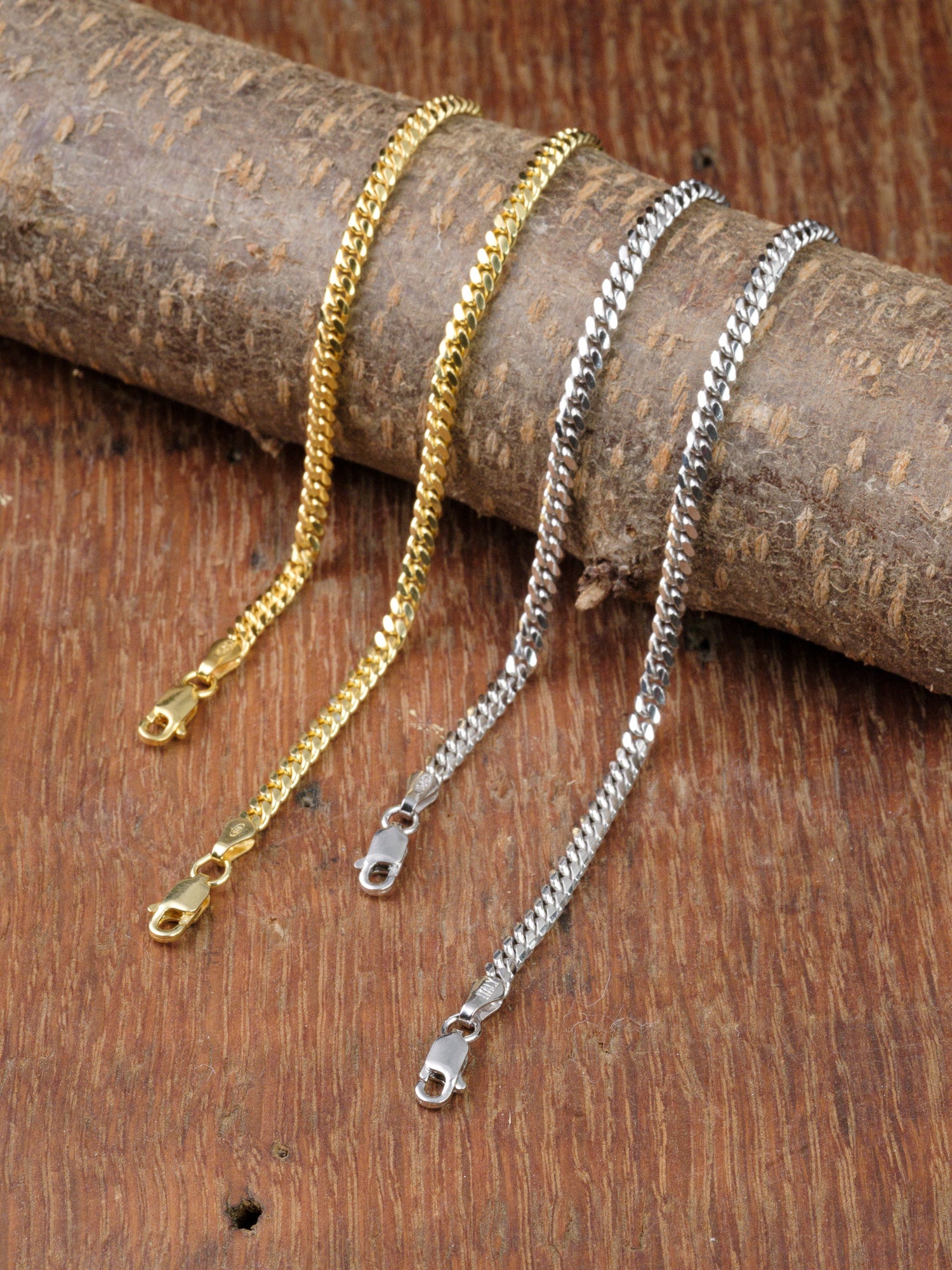 The Blaze 100 Miami Cuban Bracelet by ID Menswear is displayed side by side with a sterling silver chain on rustic wood, both featuring secure lobster claw clasps against a wooden background.