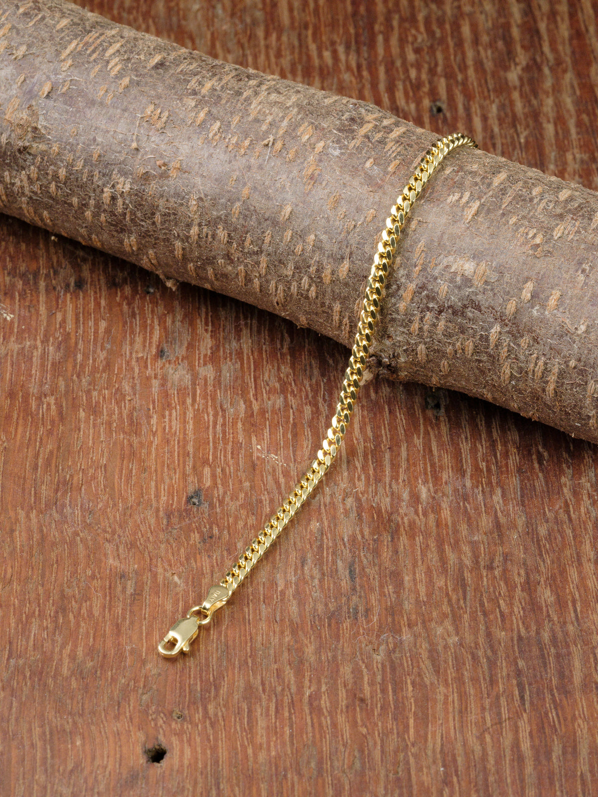 The Blaze 100 Miami Cuban Bracelet by ID Menswear, featuring a gold finish and lobster clasp, rests on wood with a wooden background.