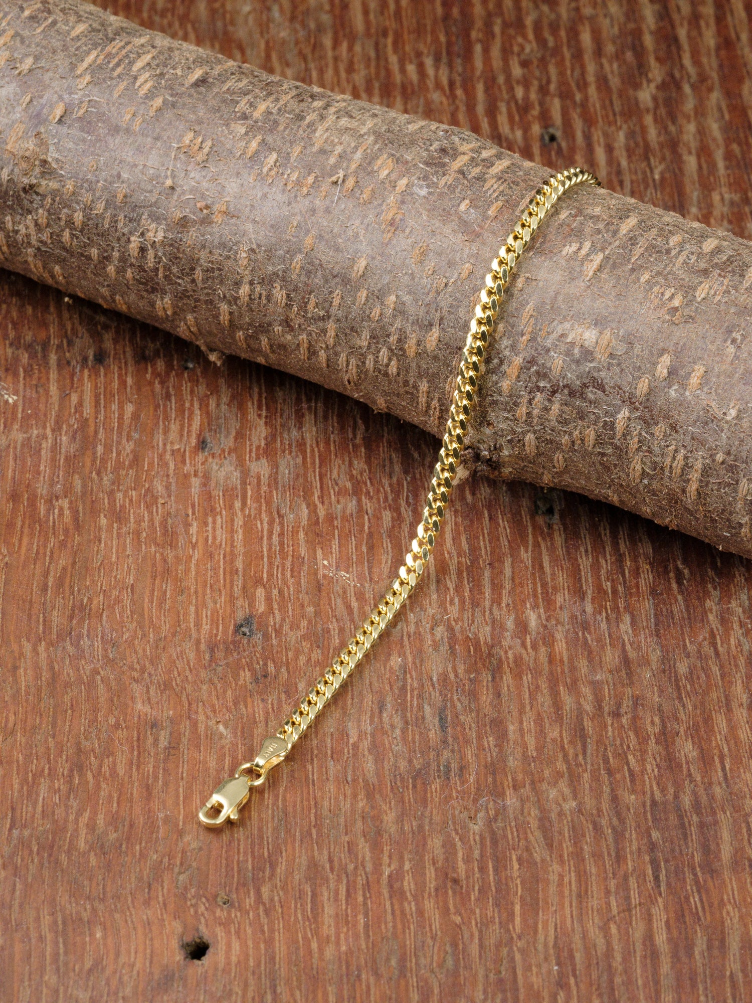 The Blaze 100 Miami Cuban Bracelet by ID Menswear, featuring a gold finish and lobster clasp, rests on wood with a wooden background.