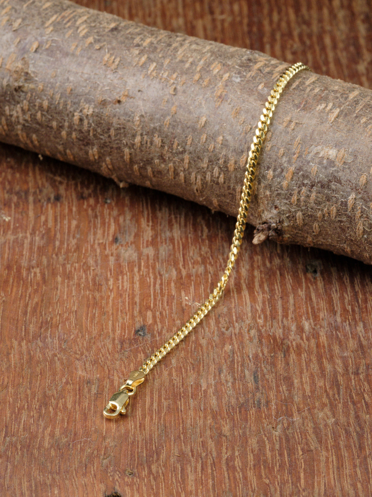 The Blaze 80 Miami Cuban Bracelet by ID Menswear, featuring a gold-plated chain and lobster clasp, is displayed draped over textured wood.