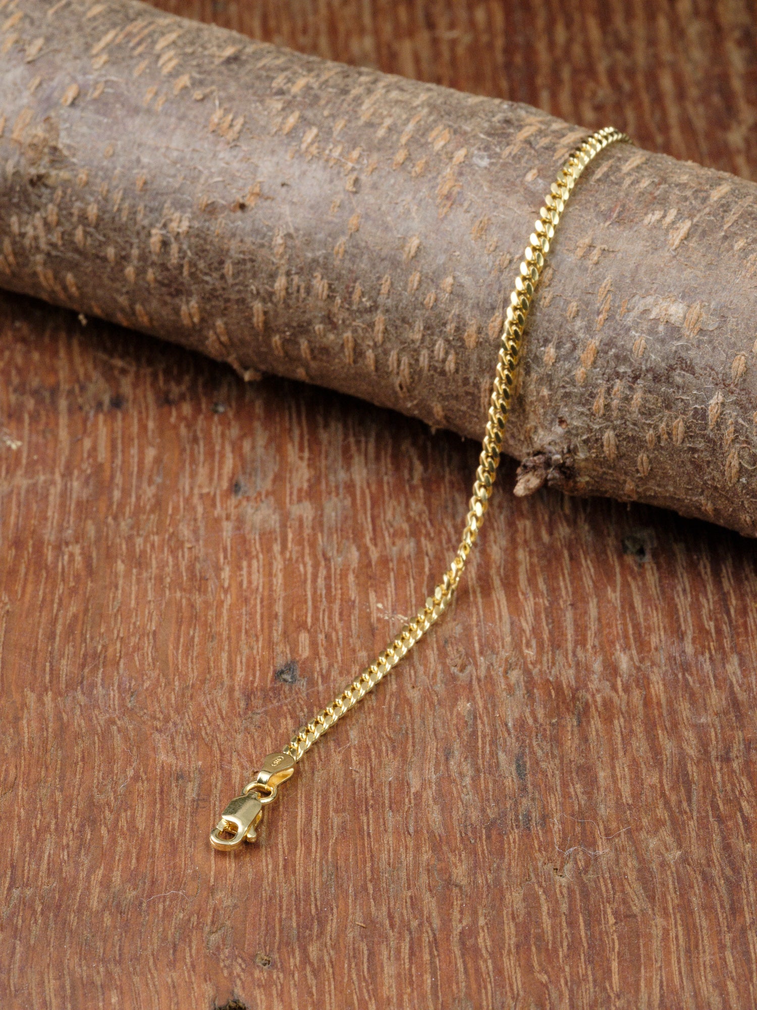 The Blaze 80 Miami Cuban Bracelet by ID Menswear, featuring a gold-plated chain and lobster clasp, is displayed draped over textured wood.