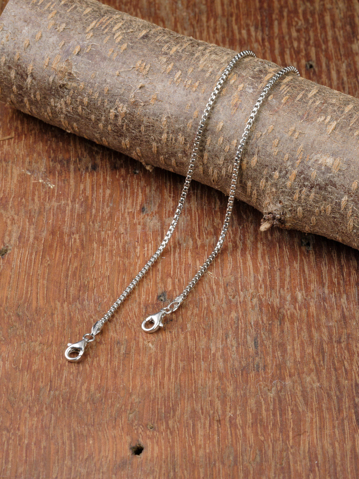 The Ezra 35 Bracelet by ID Menswear is displayed on a rustic wooden surface, with part of the bracelet draped over a textured branch.