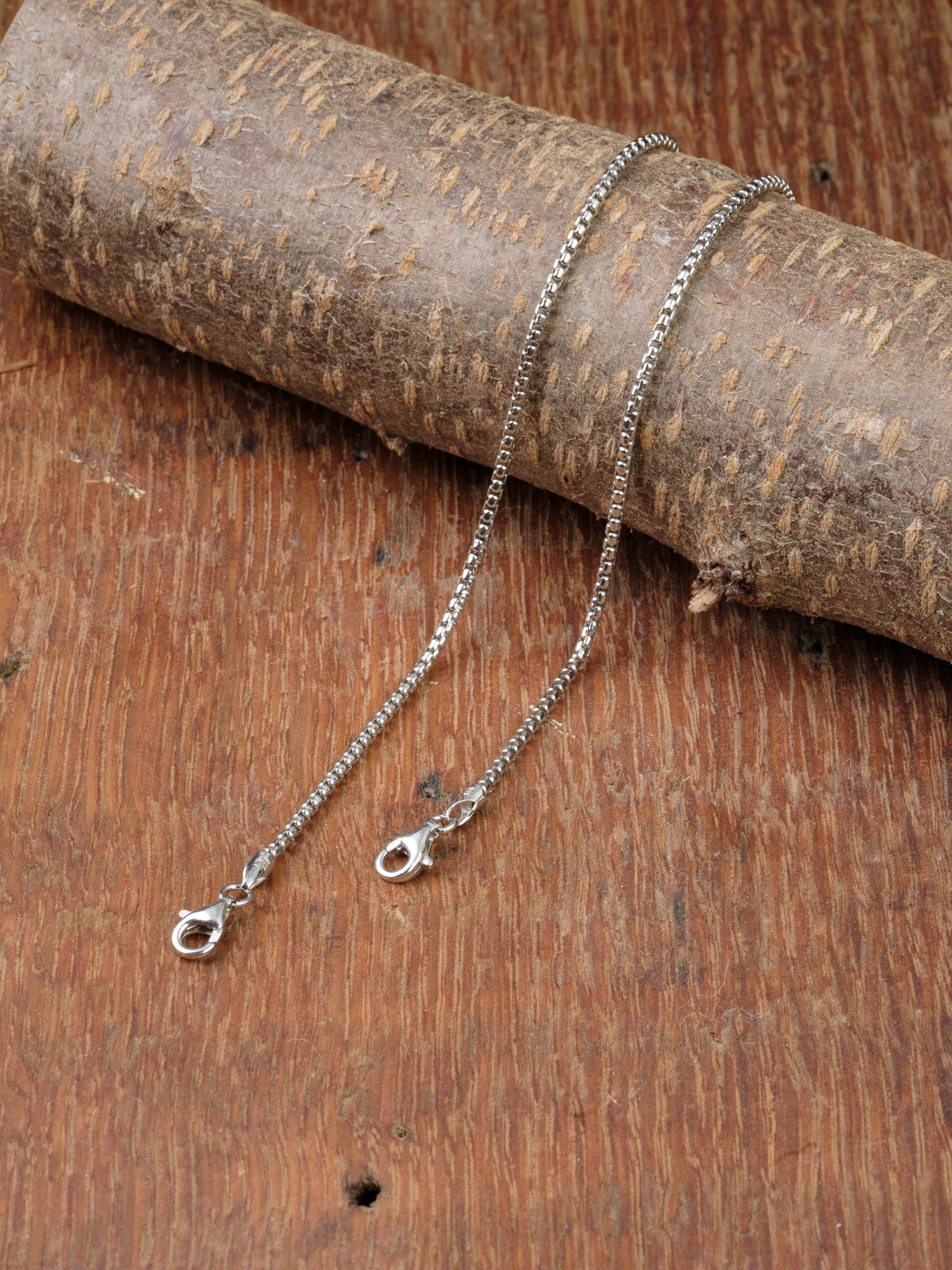 The Ezra 35 Bracelet by ID Menswear is displayed on a rustic wooden surface, with part of the bracelet draped over a textured branch.