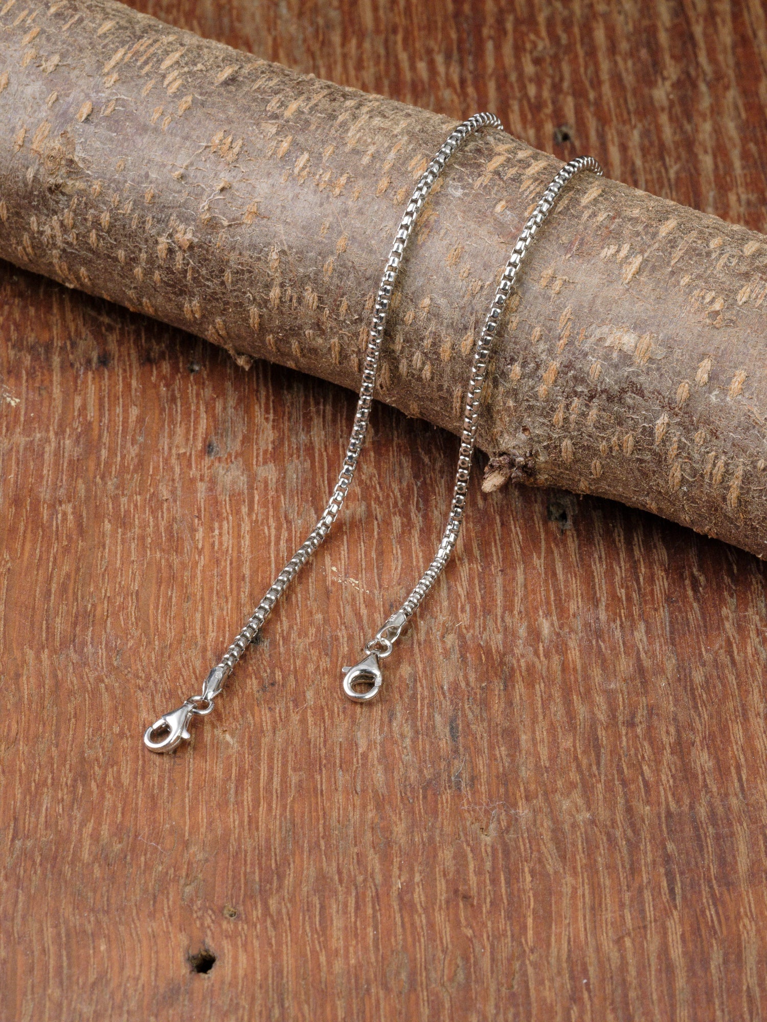 The Ezra 40 Bracelet by ID Menswear is displayed on a rustic wooden surface, with part of the chain draped over a thick wooden branch. Made in Italy, this sterling silver piece embodies timeless elegance.