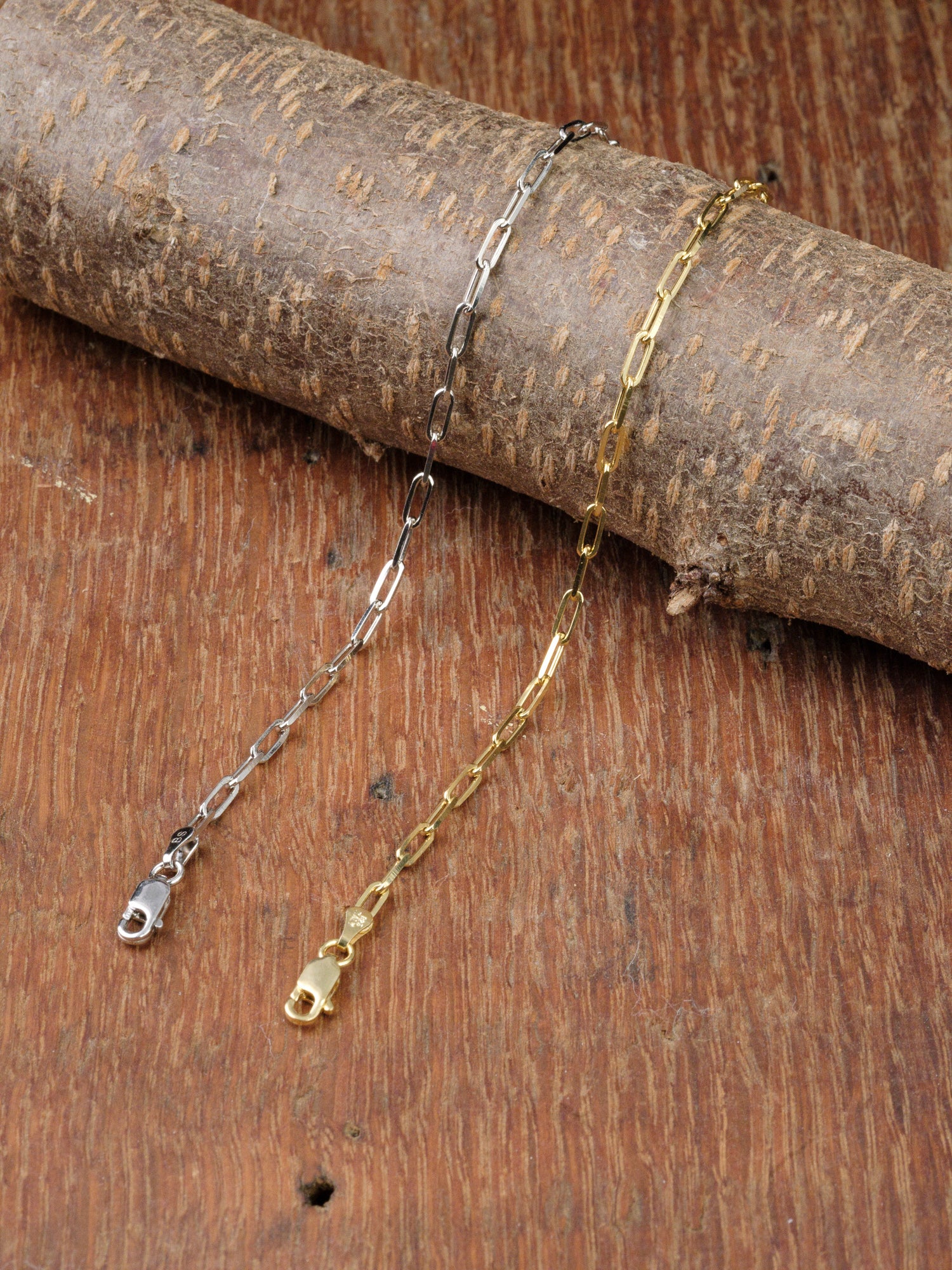 The Kai 80 Bracelet by ID Menswear, featuring oval links and a lobster clasp, is displayed on a rough wooden branch against a wooden surface background.