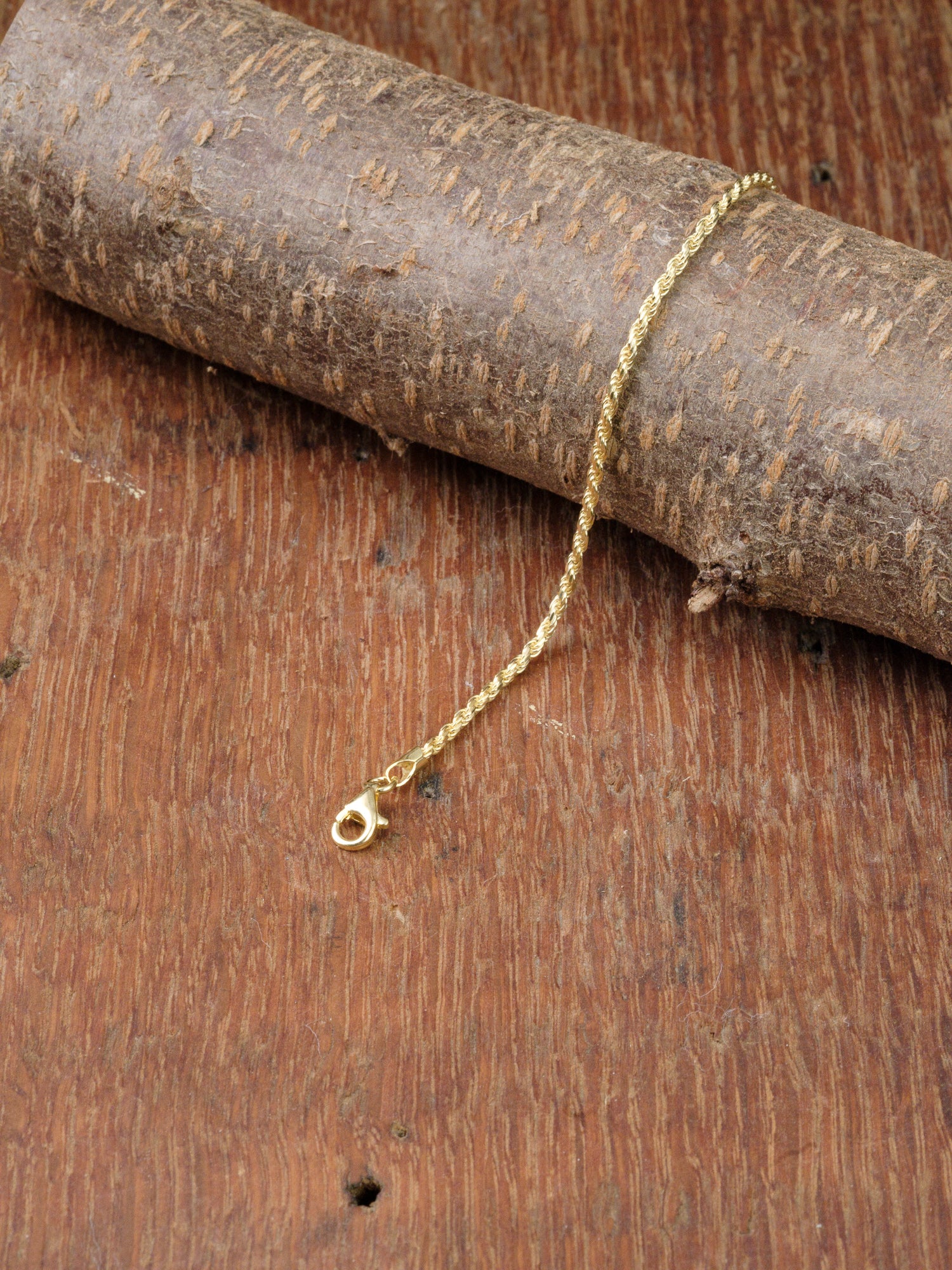 The Orion 40 Bracelet by ID Menswear, exquisitely crafted in Italy, features a gold-plated finish and lobster clasp—displayed on textured wood for a touch of timeless elegance.