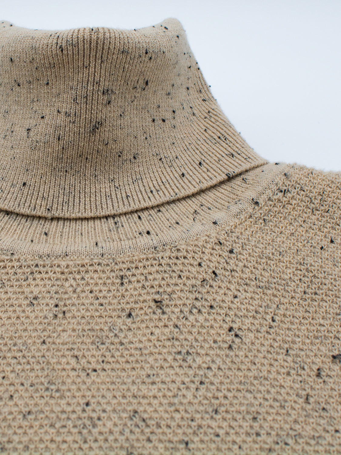 Close-up of ID Menswears Brampton High Neck Cotton Sweater: features a beige high-neck design and waffle-like texture. Speckled yarn with black flecks creates a soft, comfortable fabric ideal for cold weather.