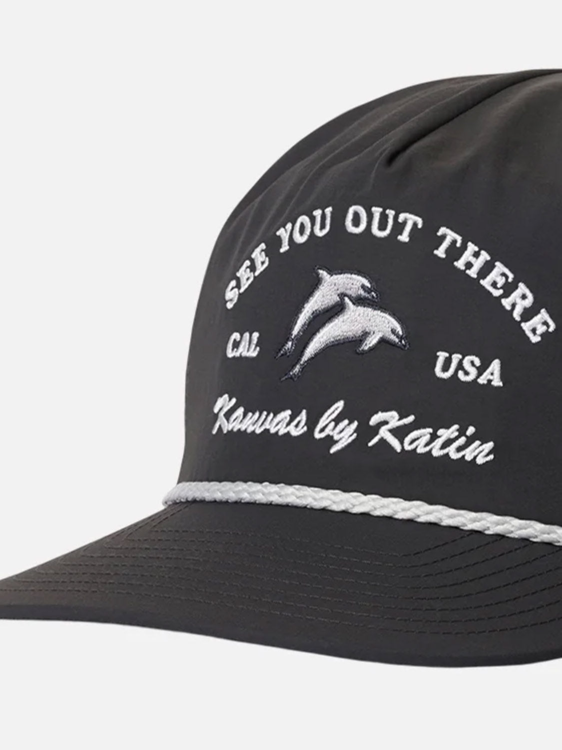The Katin Breach Hat is a black 5-panel cap made from recycled nylon, featuring white Katin embroidery with two dolphins, "SEE YOU OUT THERE," "CAL USA," "Kanvas by Katin," and a white braided band above the brim.