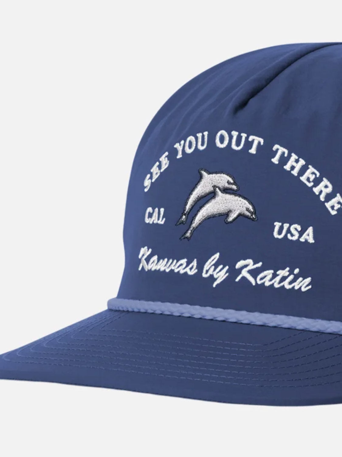 The Katin Breach Hat is a blue recycled nylon cap with Katin embroidery, "SEE YOU OUT THERE, CAL USA" text, and two dolphins at the center. It features a decorative blue rope above the brim and an adjustable snapback closure.