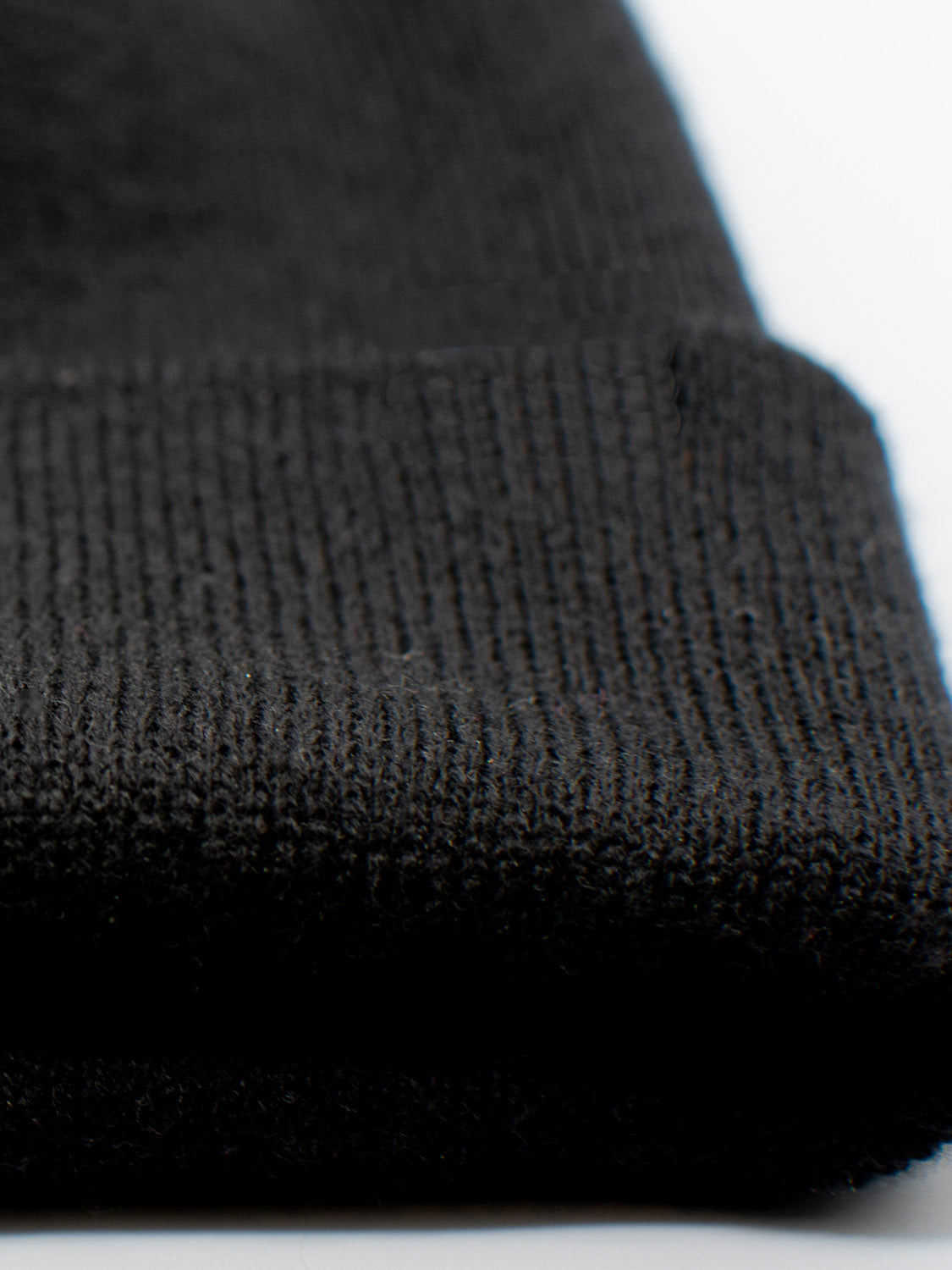 A close-up of a black knitted fabric with a folded edge resembles the Bronx Acrylic Beanie by ID Menswear, highlighting its detailed weaving pattern. The soft and slightly textured fabric embodies the beanies stretchable design essence.