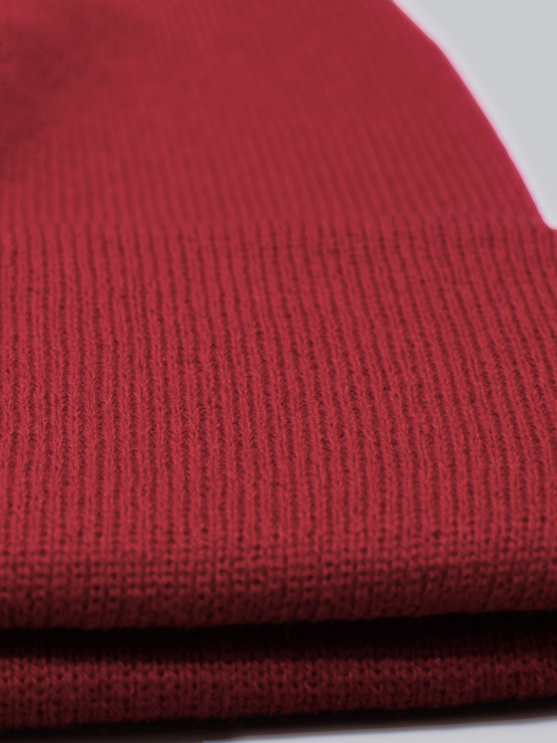 Close-up of a folded red Bronx Acrylic Beanie by ID Menswear, highlighting its ribbed texture and stretchable design. The image emphasizes the fabric and stitching, conveying warmth and comfort.