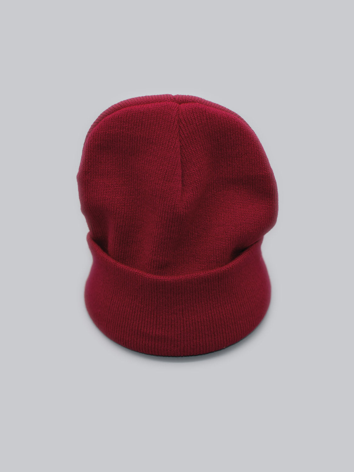 A red Bronx Acrylic Beanie from ID Menswear, featuring a folded brim and stretchable design, rests against a gray background.