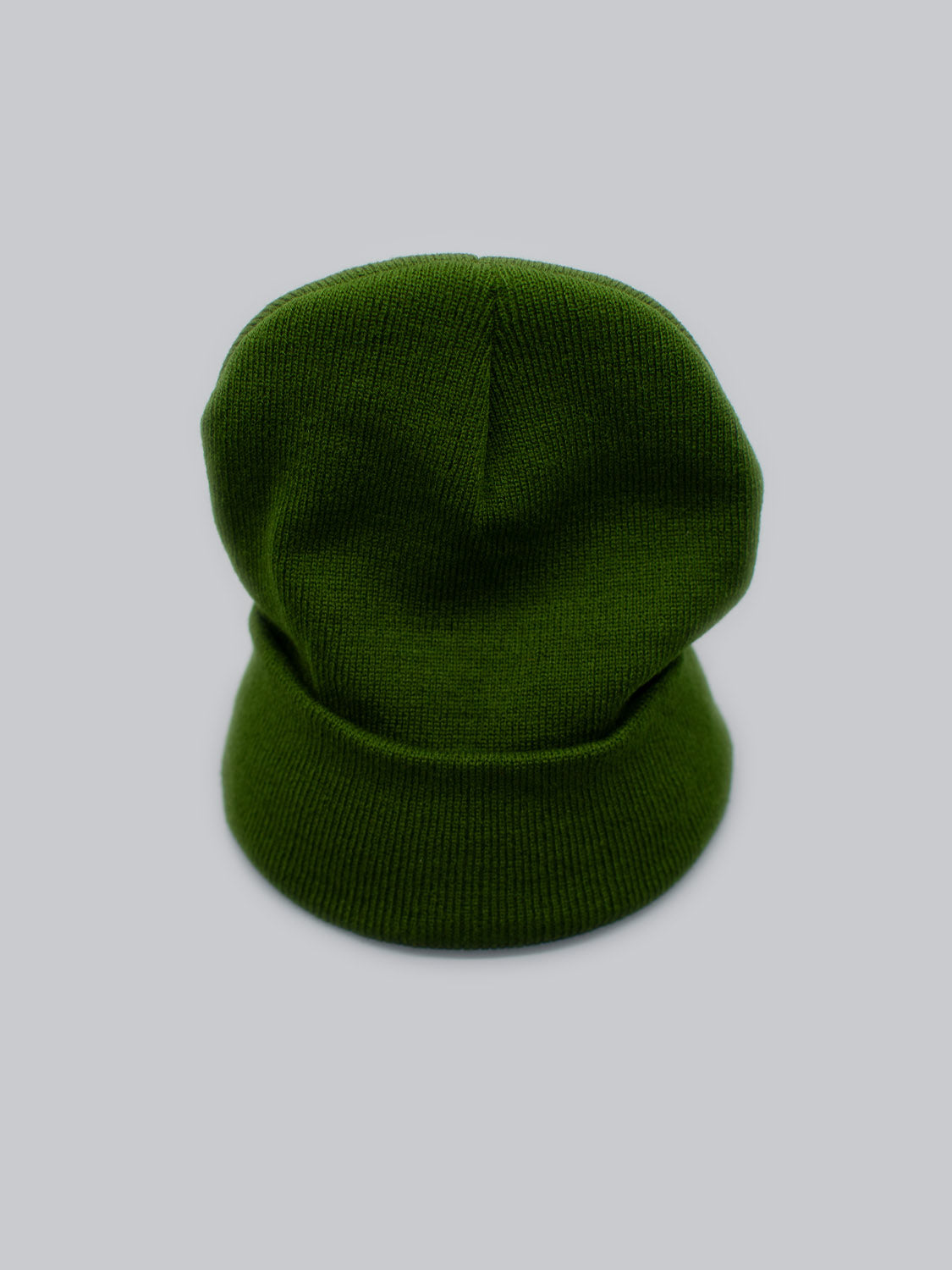 The Bronx Acrylic Beanie by ID Menswear, a green knitted hat with a folded brim, is set against a solid light gray background. Its stretchable design ensures a perfect fit while showcasing texture and simple elegance.