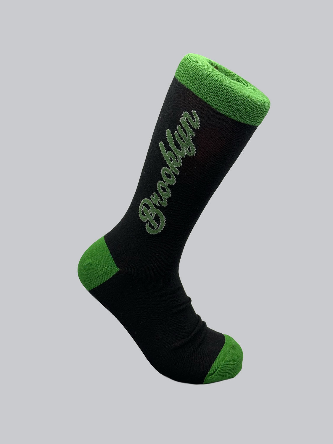 These Brooklyn Graphic Socks by ID Menswear feature Brooklyn in green cursive on black, with green accents on the toe, heel, and top cuff set against a plain grey background. Crafted from premium materials for comfort and style versatility.