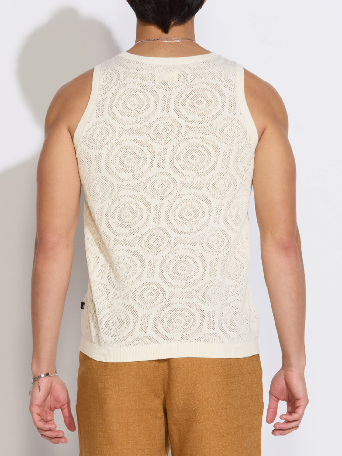 A person is seen from behind wearing the Civil Society Buyugo Sweater Knit Tank Top—a sleeveless, white crochet-style geometric tank—paired with light brown pants against a plain white background.