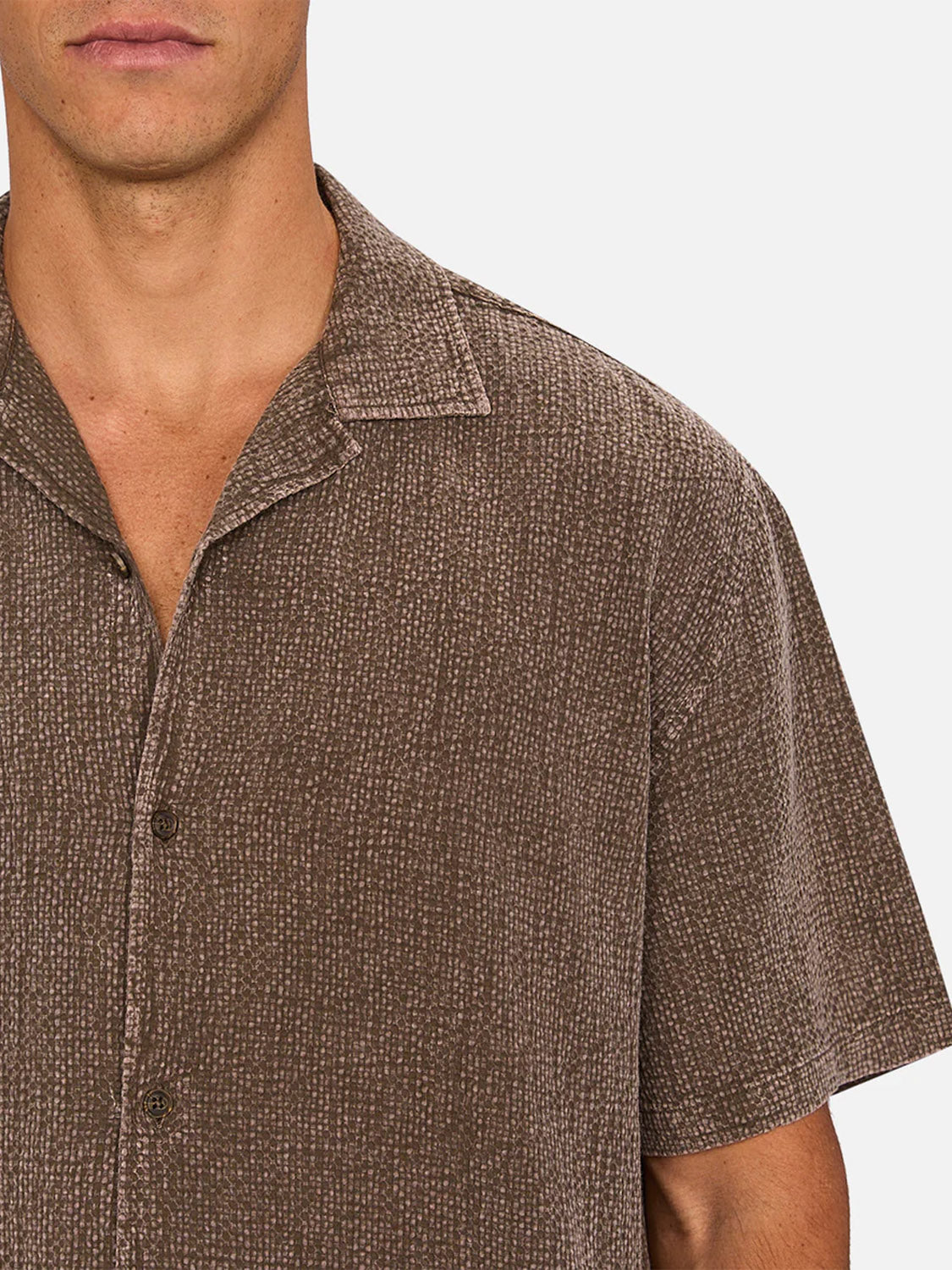 A man models The Canyon Short Sleeve Shirt by Industrie, a brown lightweight summer shirt with a textured pattern and relaxed fit, shown from shoulders to mid-chest against a plain white background.