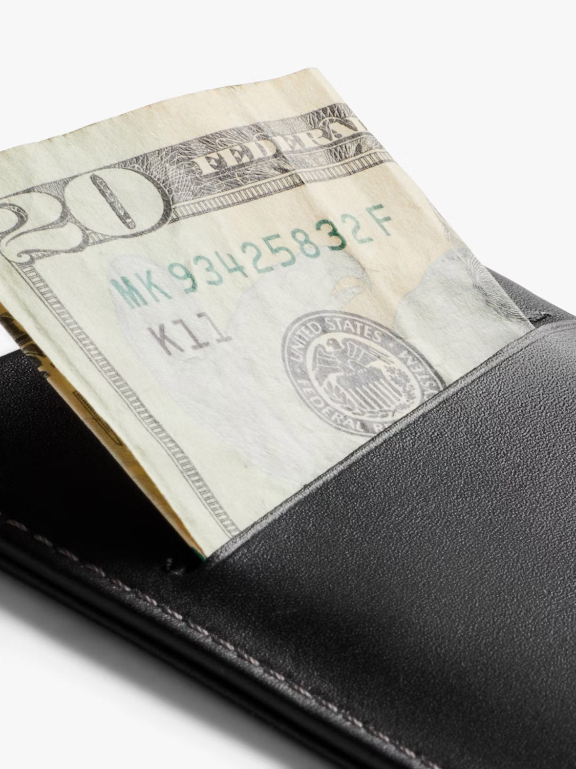 A close-up of the Bellroy Card Sleeve Wallet, crafted from premium leather, with a partially visible twenty-dollar bill tucked inside against a white background.