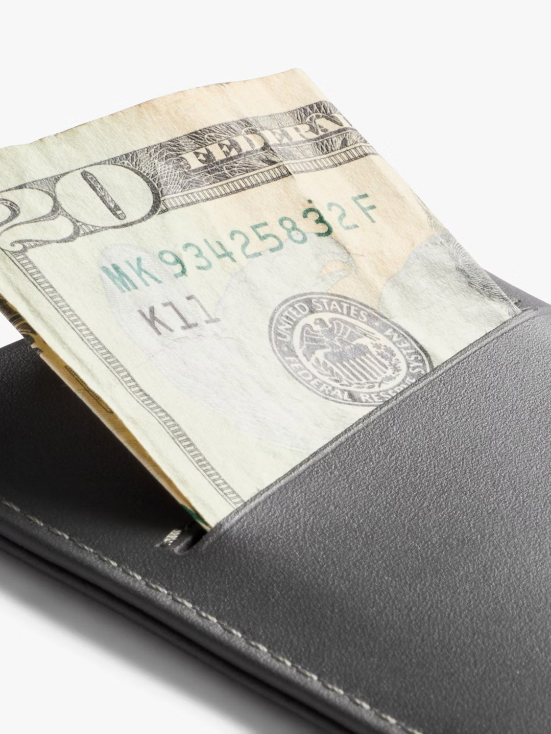 A close-up of a Bellroy Card Sleeve Wallet in black, featuring a partially visible folded U.S. twenty-dollar bill, set against a plain white background.