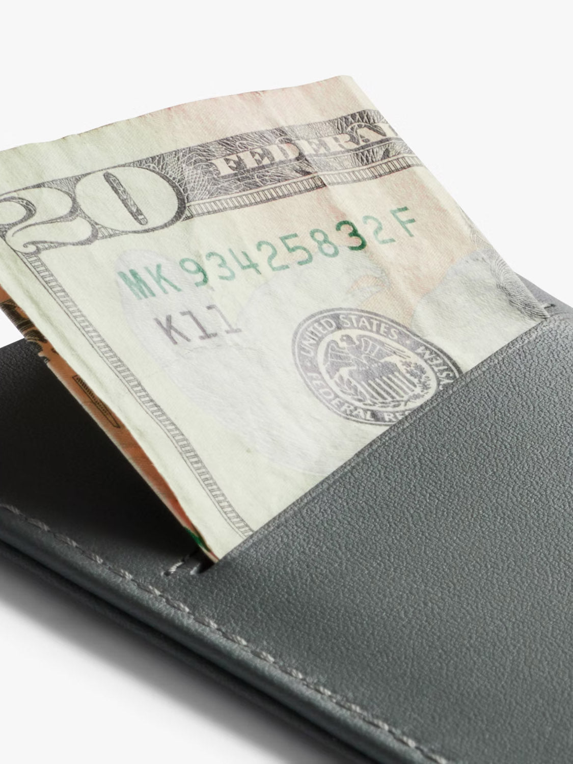 A close-up of the Bellroy Card Sleeve Wallet, a minimalist black leather accessory, with a folded U.S. twenty-dollar bill partially visible against a plain white background.