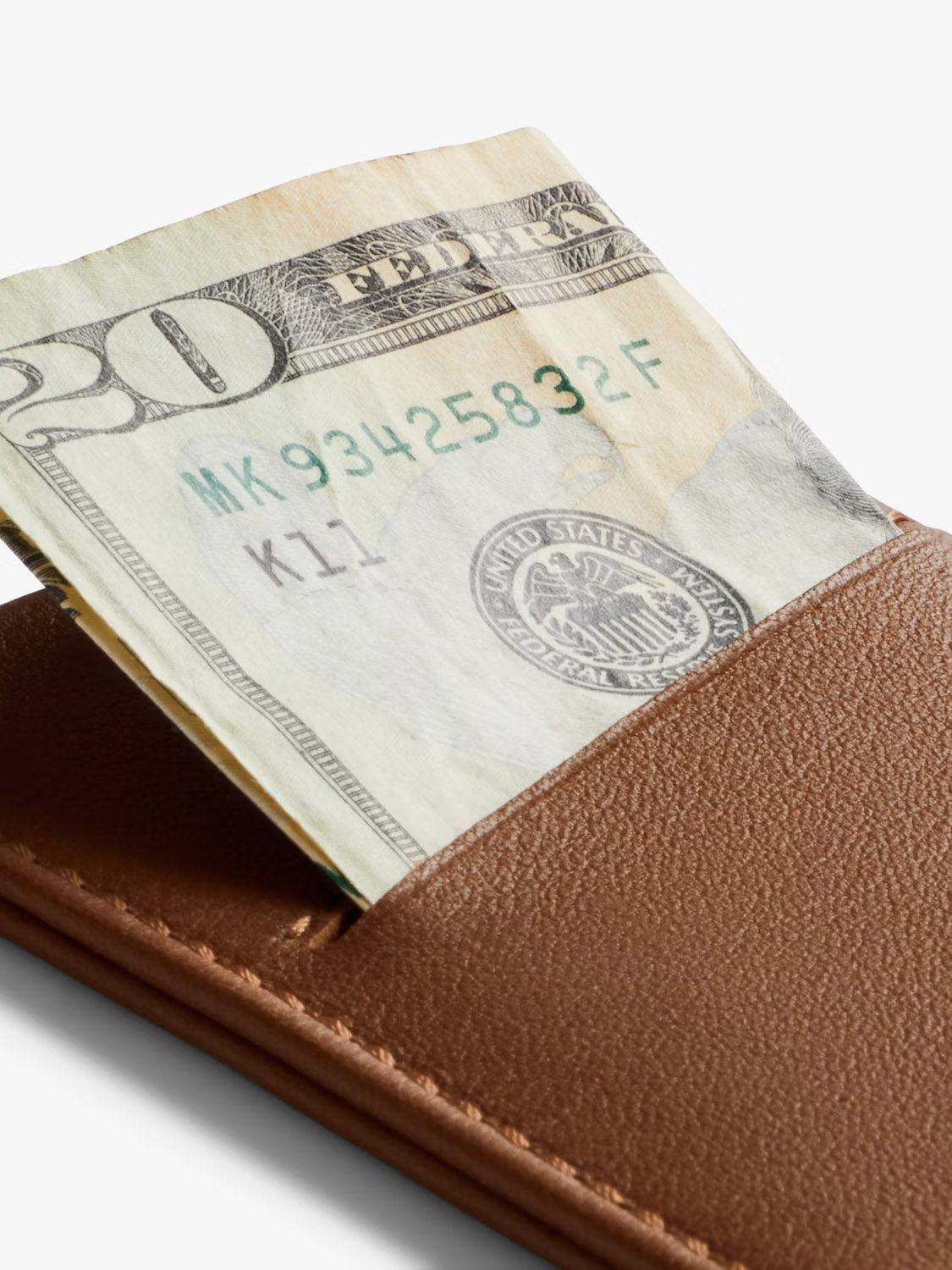 A close-up of a twenty-dollar bill partially sticking out of a Bellroy Card Sleeve Wallet against a white background.