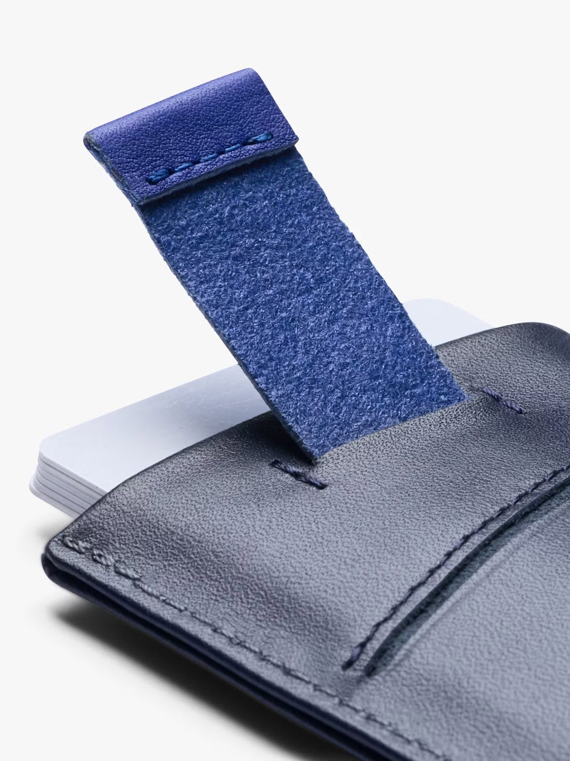 A close-up of the Bellroy Card Sleeve Wallet in navy leather, featuring a blue pull tab and partially showing white cards inside—a slim, stylish solution for carrying your everyday essentials.