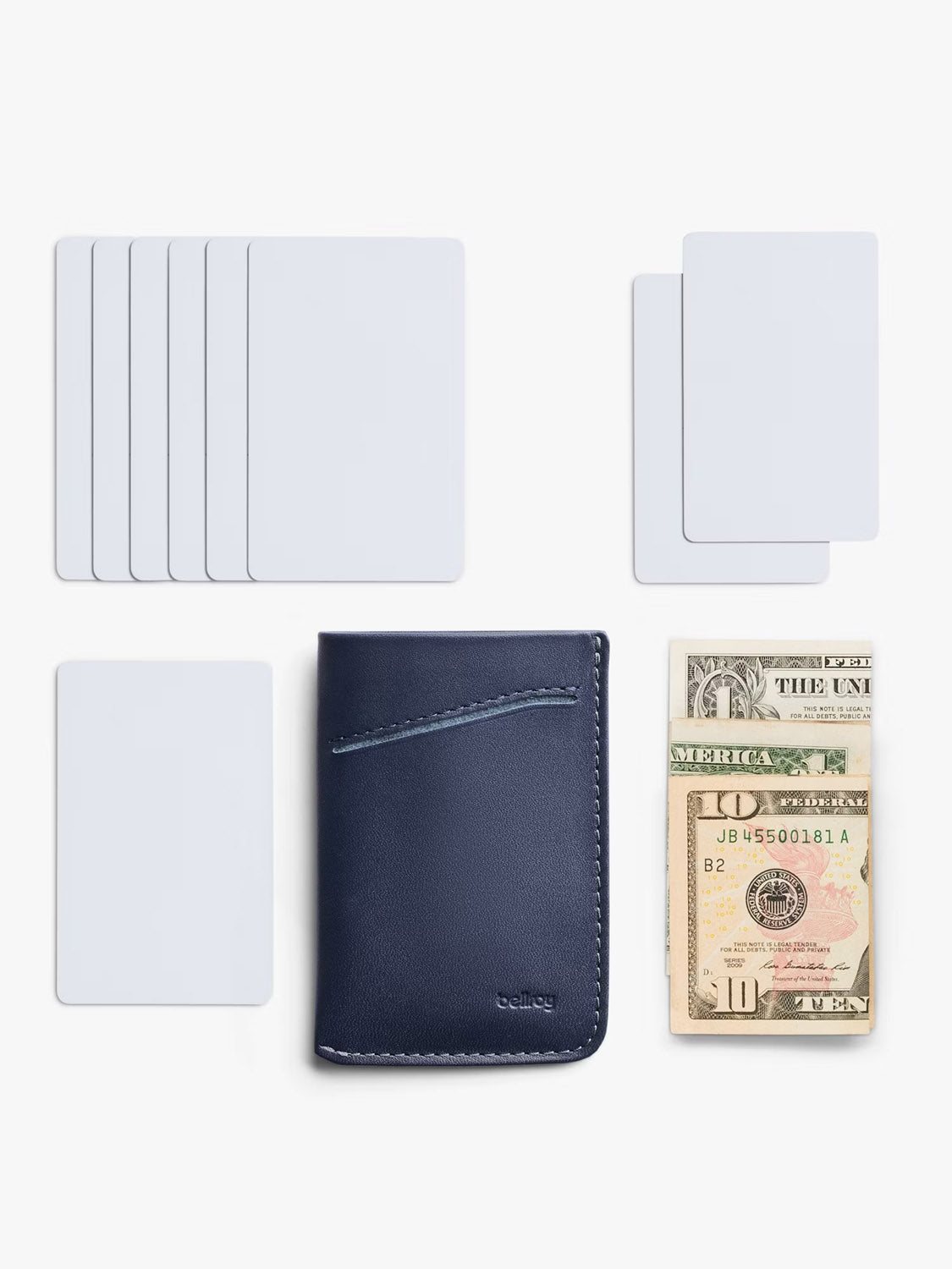 A Bellroy Card Sleeve Wallet in navy blue sits next to blank white cards and folded U.S. dollar bills, all neatly arranged on a white background.