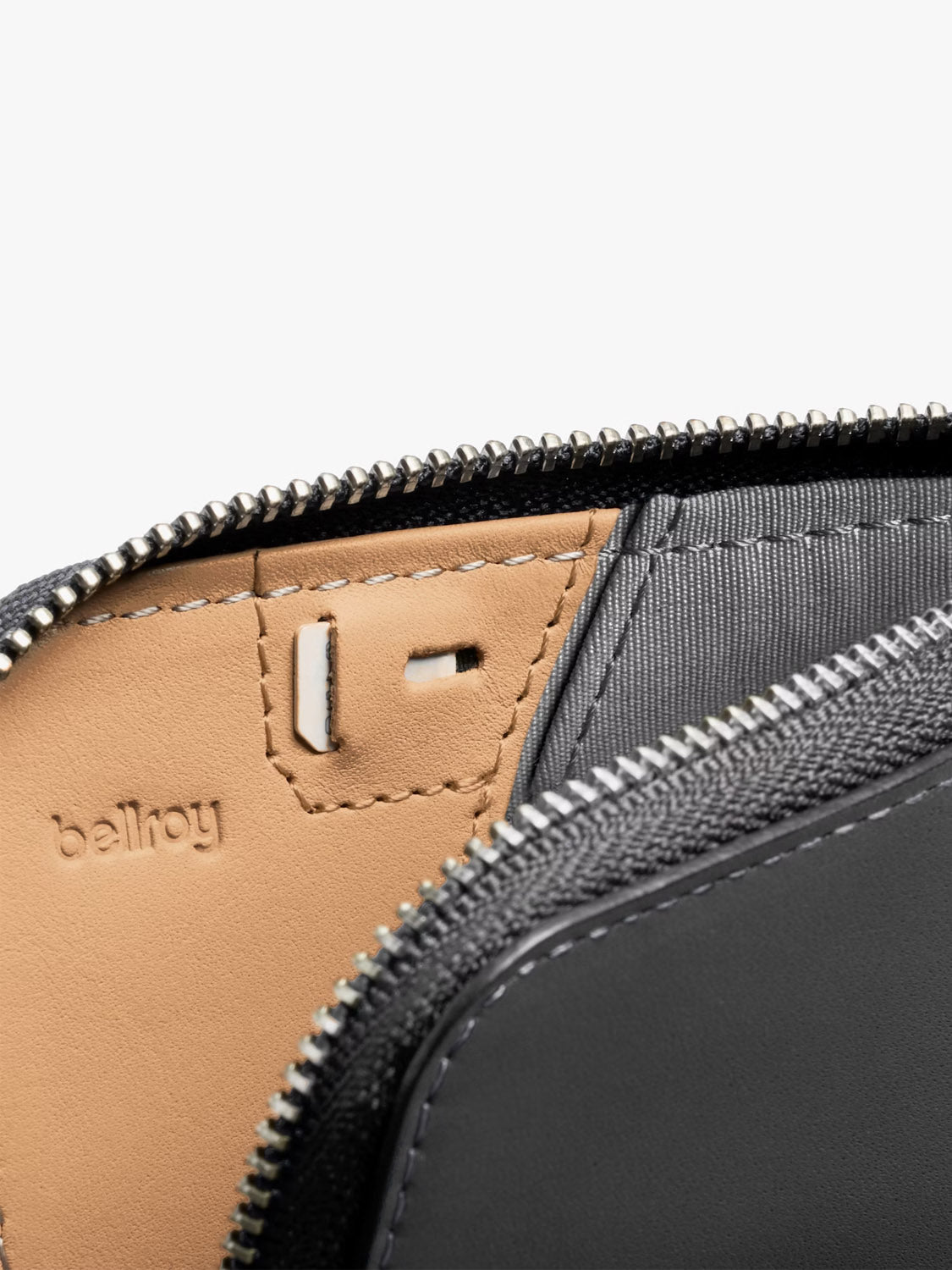 Close-up of the Bellroy Card Pocket Wallet in black leather with a zipper, showing tan and gray lining, detailed stitching, coin pouch, and Bellroy branding embossed on the interior.