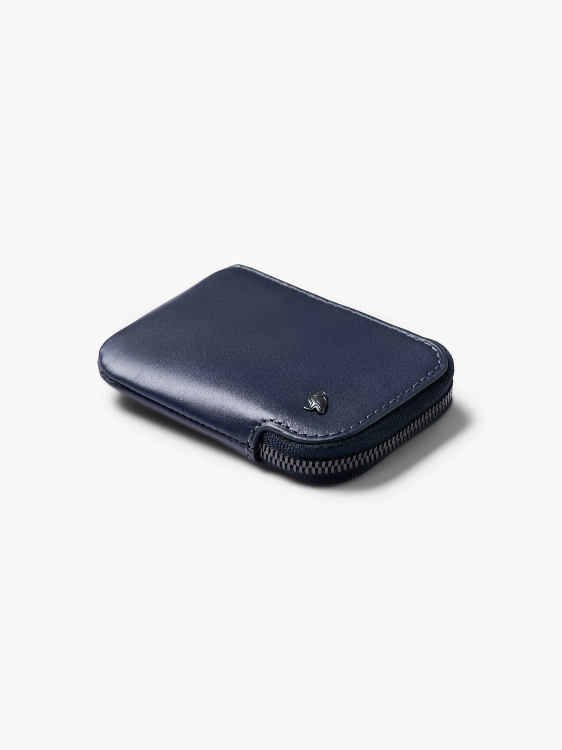 The Bellroy Card Pocket Wallet, in navy blue leather, rests closed on a light gray background, highlighting its minimalist design, convenient coin pouch, and subtle metal logo in the corner.