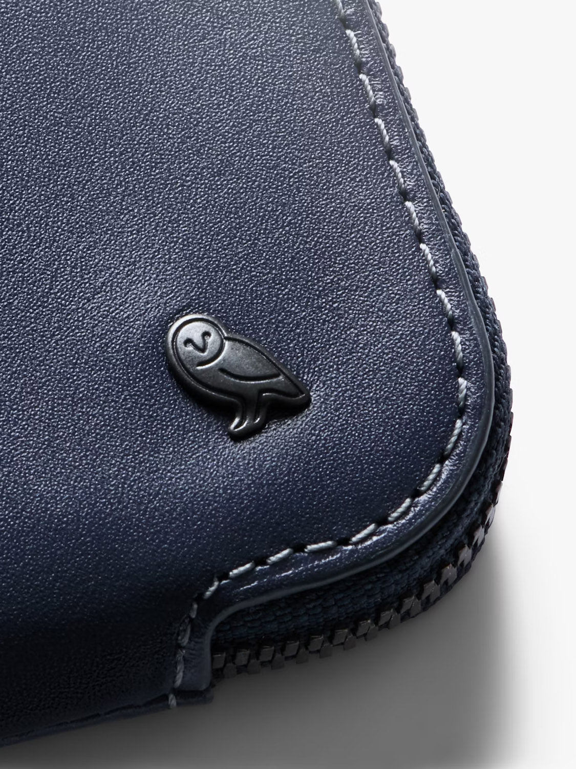 Close-up of the Bellroy Card Pocket Wallet in navy blue leather, highlighted by detailed edge stitching and a small black owl emblem.