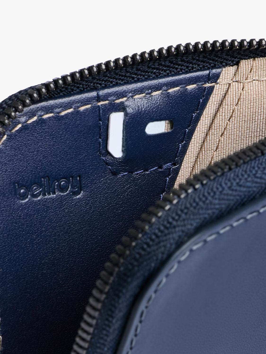 Close-up of Bellroy’s Card Pocket Wallet in navy leather shows detailed stitching, a zipper, and beige lining. The Bellroy logo is embossed on the leather, emphasizing the wallet’s thoughtful and versatile design.