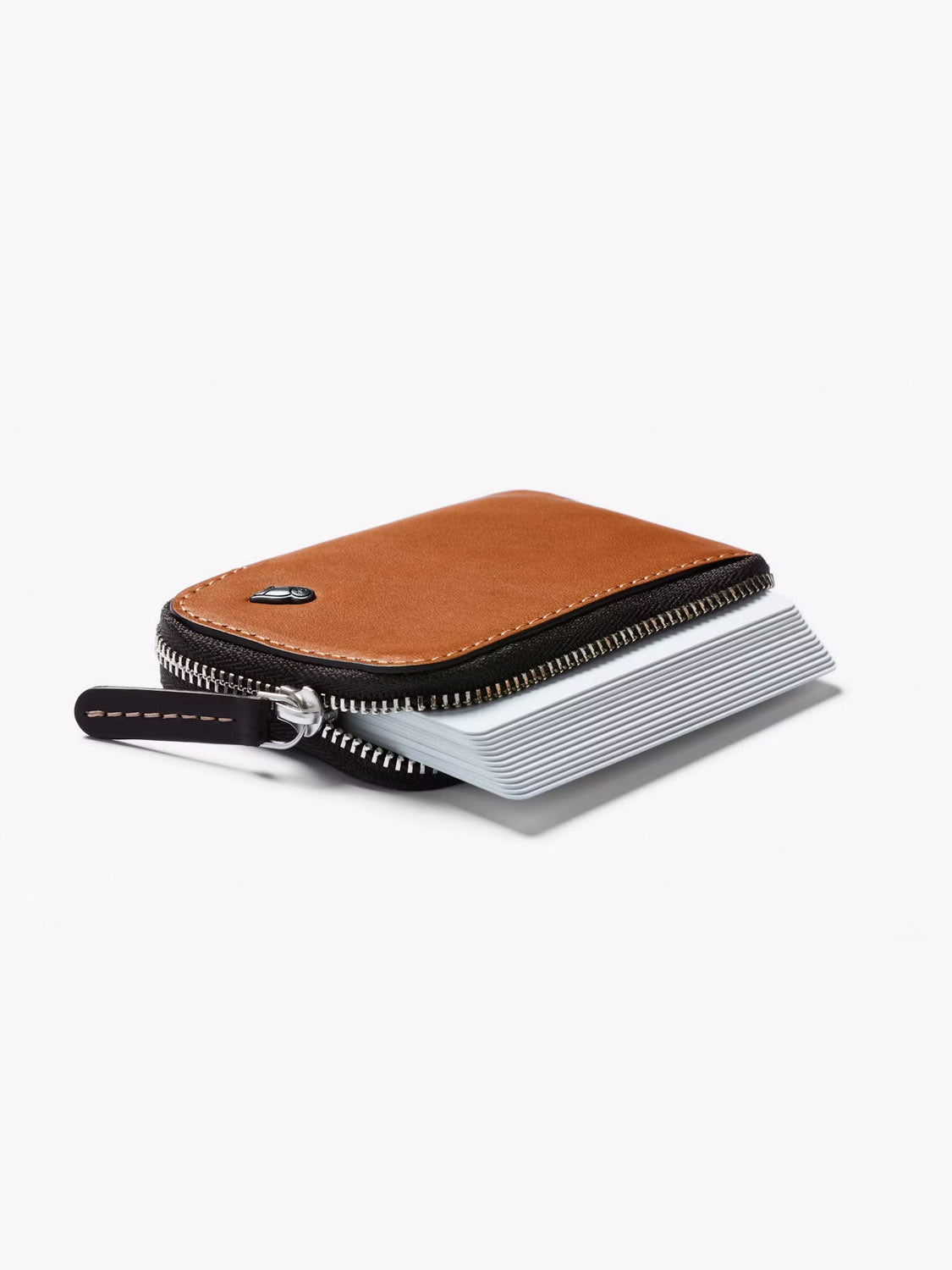 The Bellroy Card Pocket Wallet, crafted in brown leather, is partially open to show stacked cards inside. It features black edges, white stitching, and a small metallic emblem on the corner.