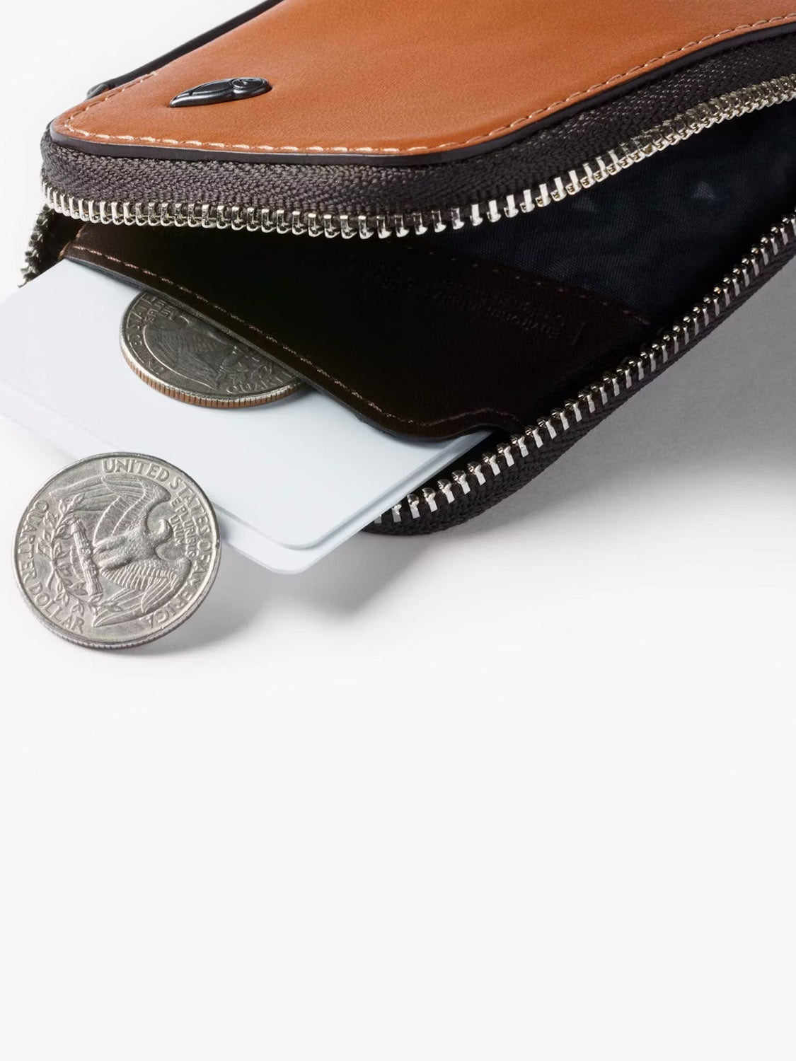 A close-up of the Bellroy Card Pocket Wallet in brown leather, partially open to show a credit card and coins—such as a U.S. quarter—set against a white background.