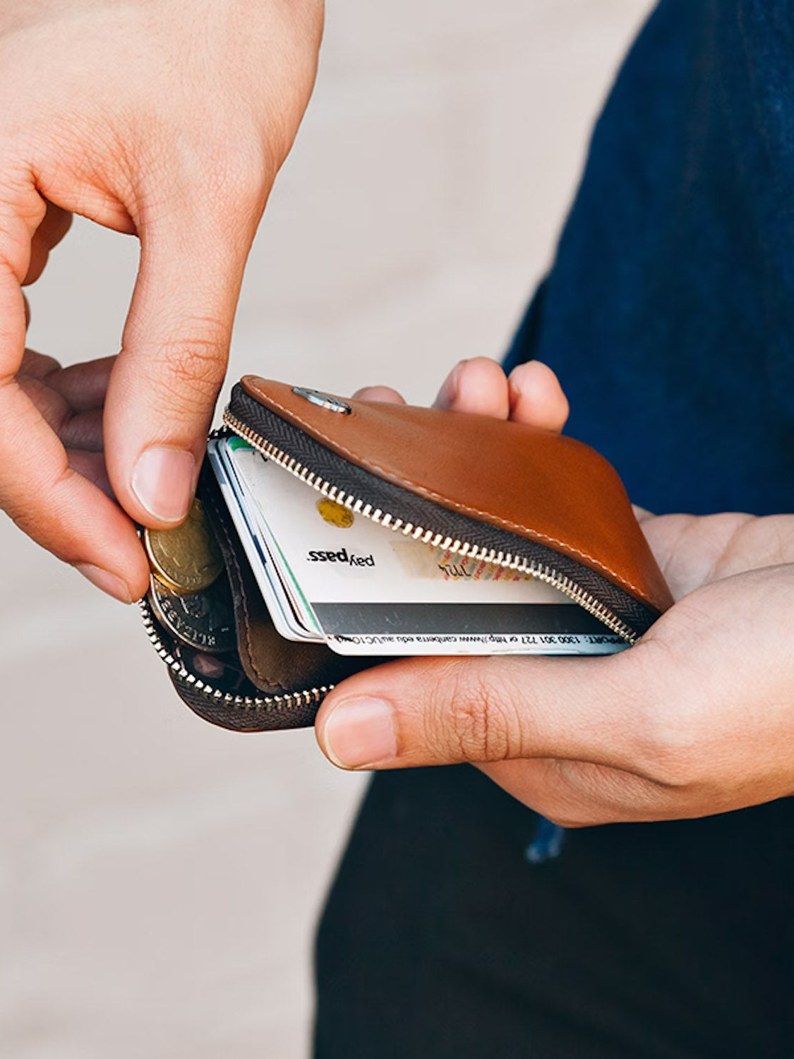 A person inserts coins into the Bellroy Card Pocket Wallet, which reveals cards and bills inside. The background is softly blurred.