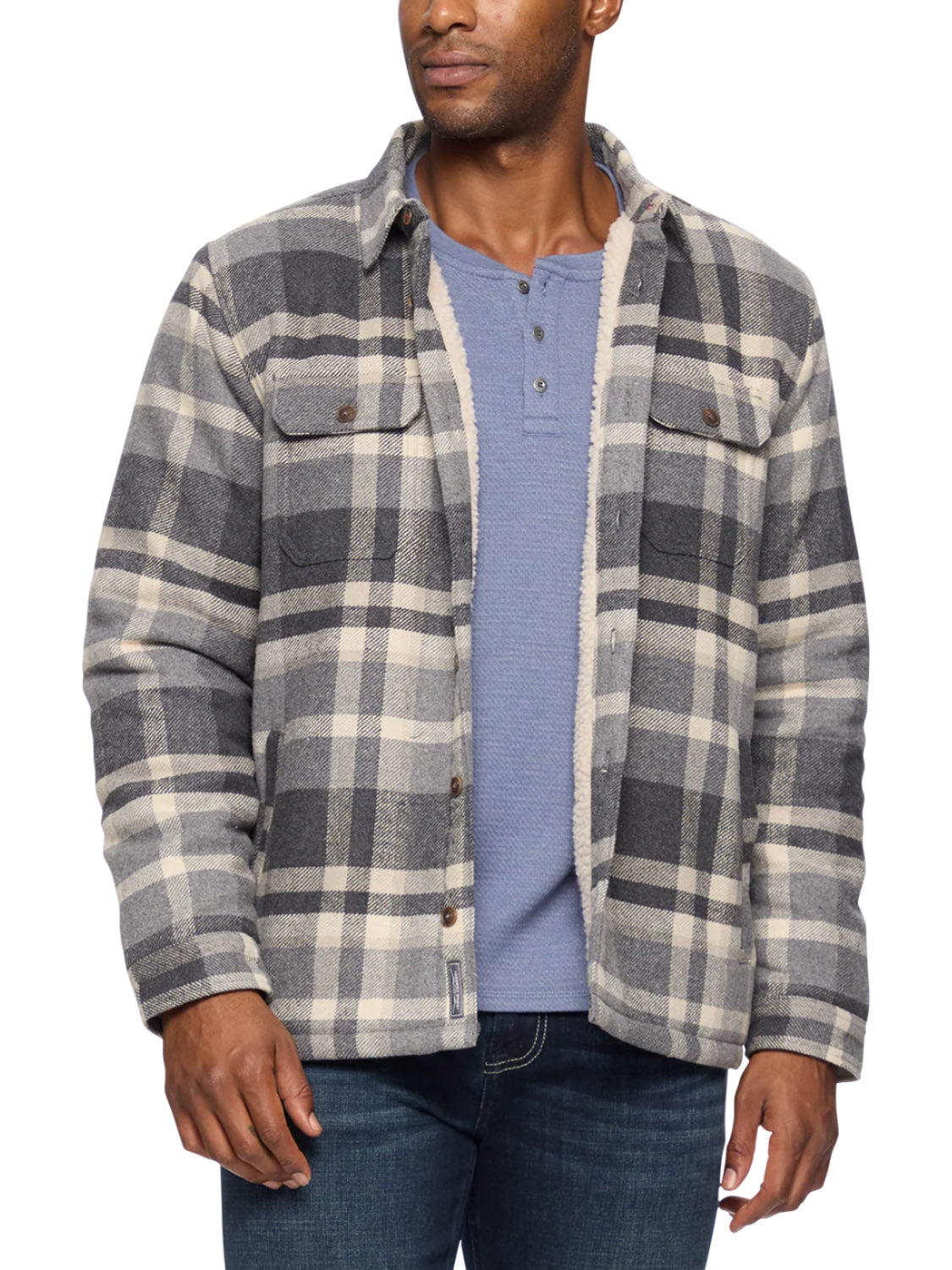 A man stands slightly turned, wearing the Flag and Anthem Cassidy Sherpa Lined Shirt Jacket in a gray, white, and black plaid pattern over a light blue henley and dark blue jeans.