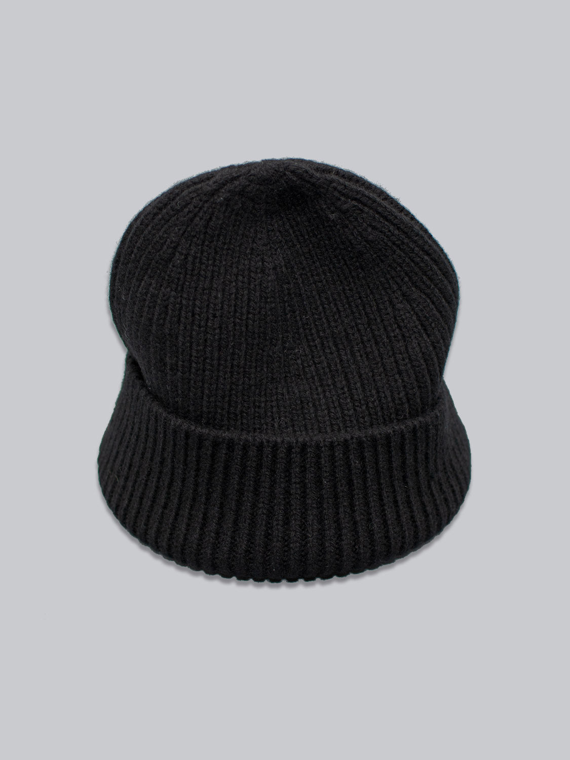 The ID Menswear Chamonix Wool Beanie, crafted from 100% wool, features a black knit with ribbed texture and folded brim. Set on a light gray backdrop, it provides natural insulation for cozy warmth in cold weather.