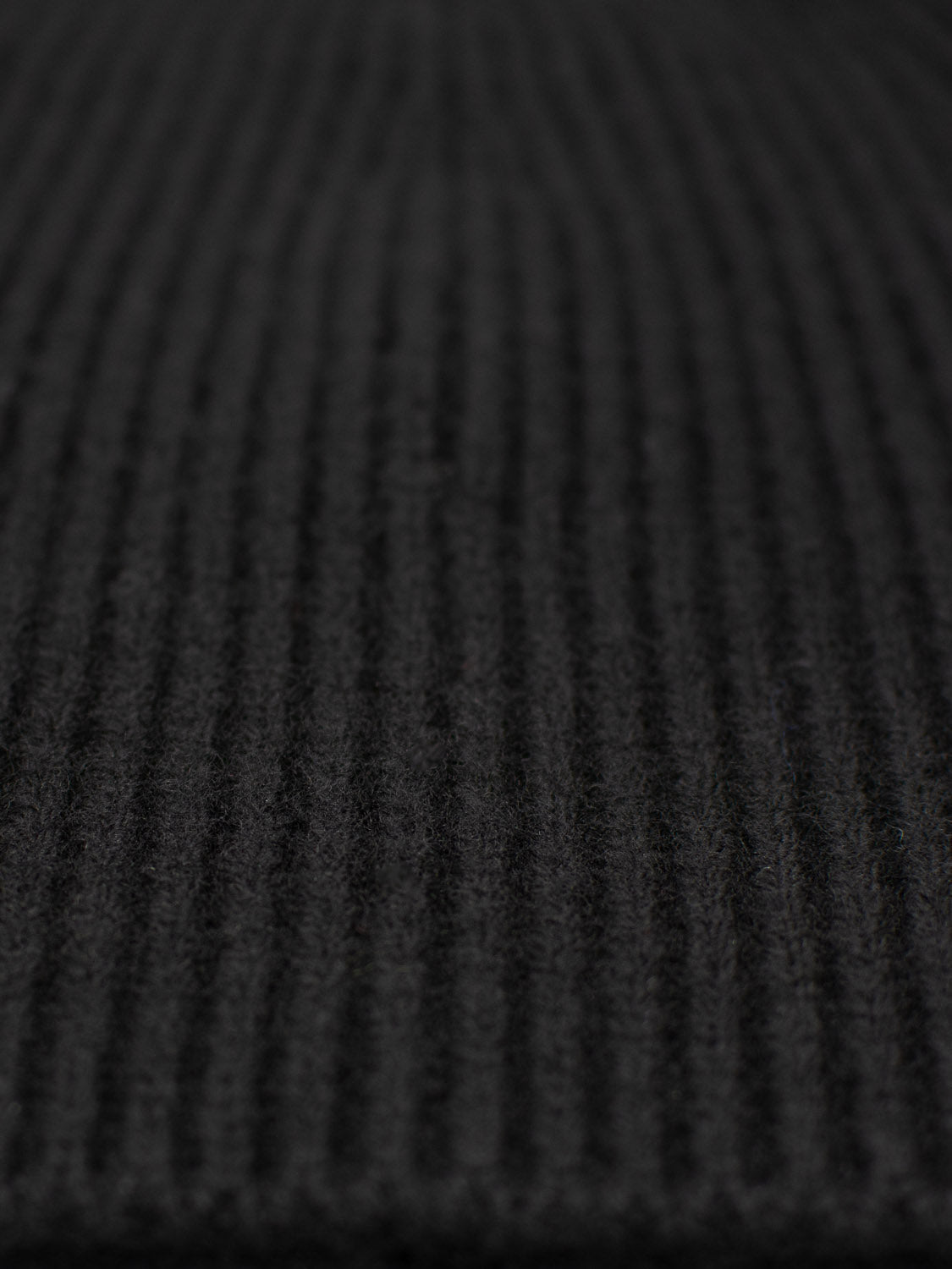 A close-up of the Chamonix Wool Beanie by ID Menswear showcases its 100% wool ribbed fabric with a soft, textured look. The vertical ridges form a distinct pattern that enhances natural insulation.