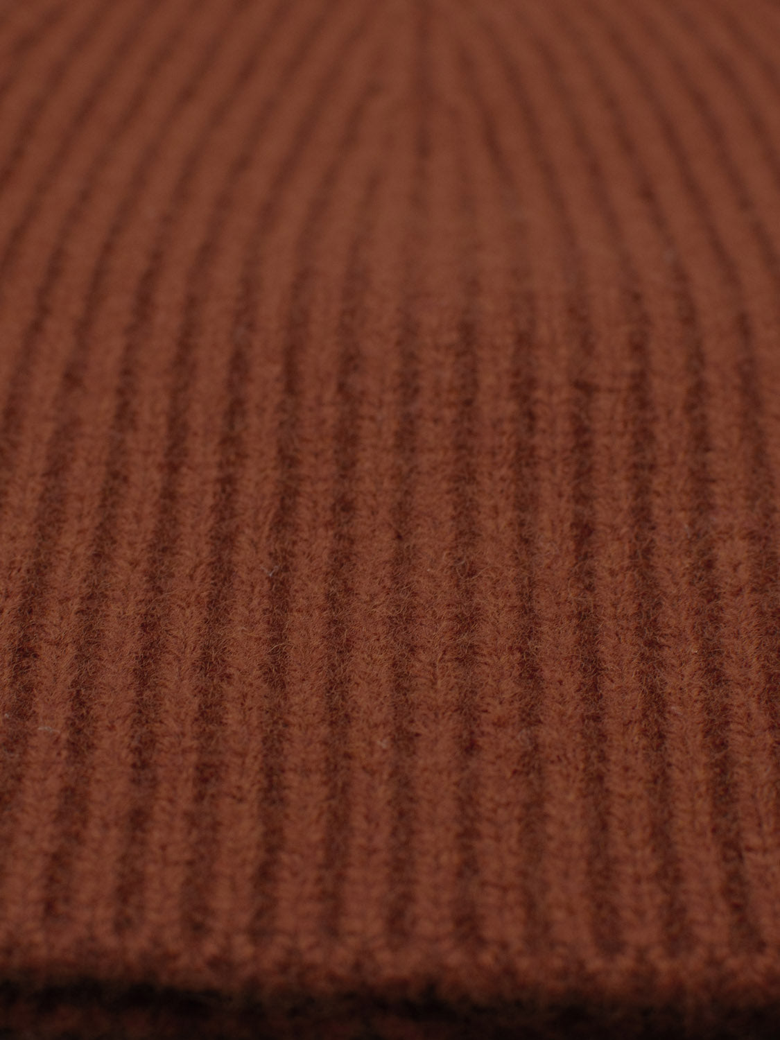 Close-up of a textured, ribbed knit fabric made from 100% wool. The vertical lines add depth and insulation, much like the Chamonix Wool Beanie by ID Menswear, featuring a warm brown hue.