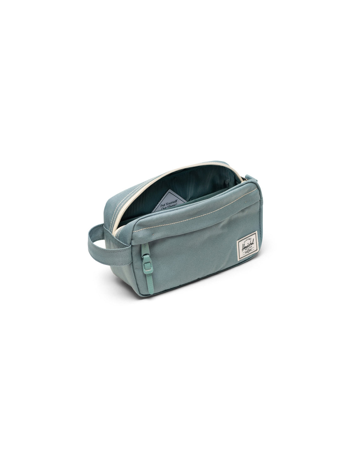 The Herschel Chapter Small Travel Kit is a light teal, eco-friendly toiletry bag featuring a zipper, side handle, white rectangular front label, and a partially open view revealing its striped interior lining.