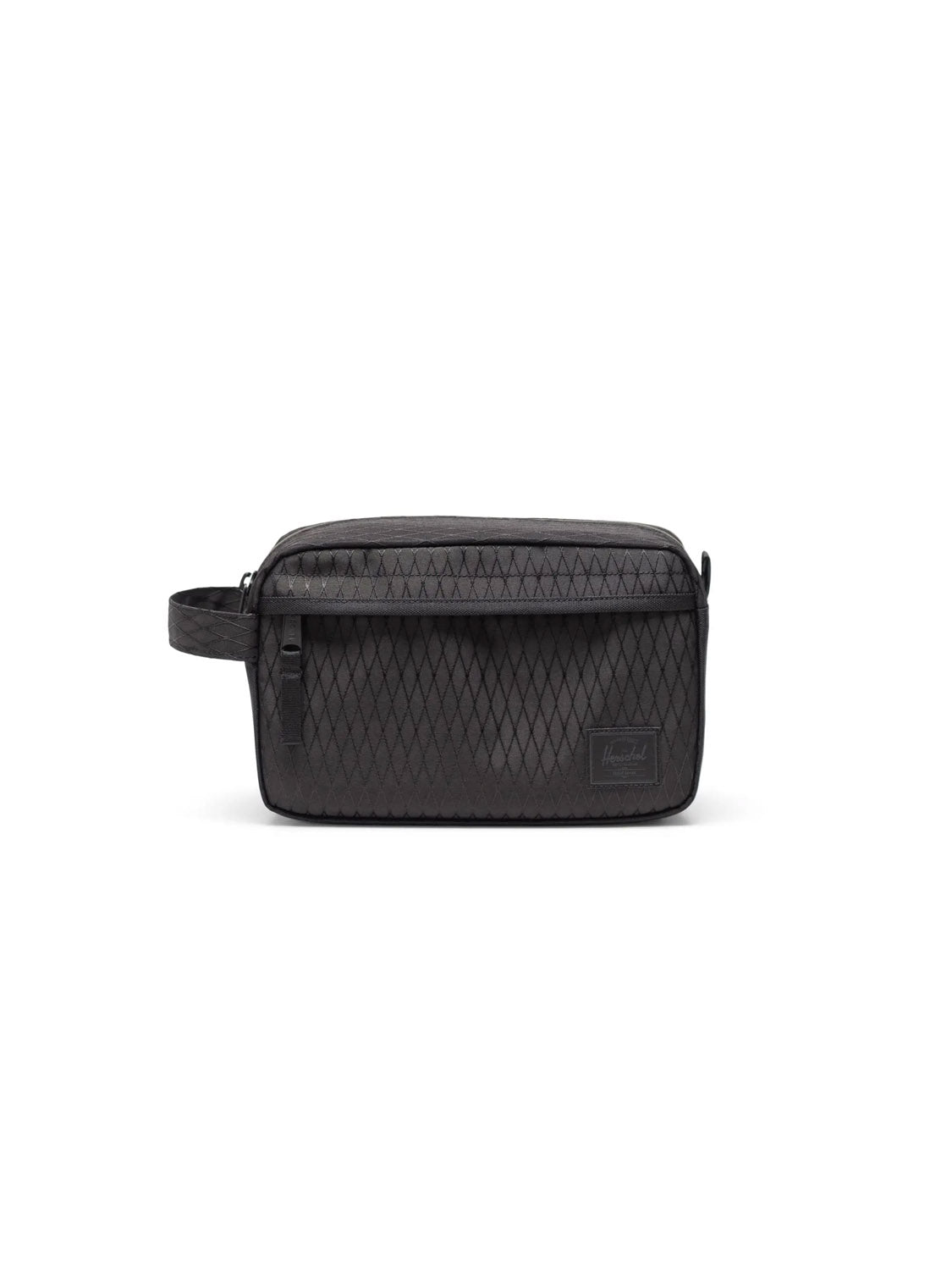 The Herschel Chapter Travel Kit - 5L is a black, rectangular toiletry bag made from recycled polyester with a diamond pattern, side handle, and front patch label, shown against a white background.
