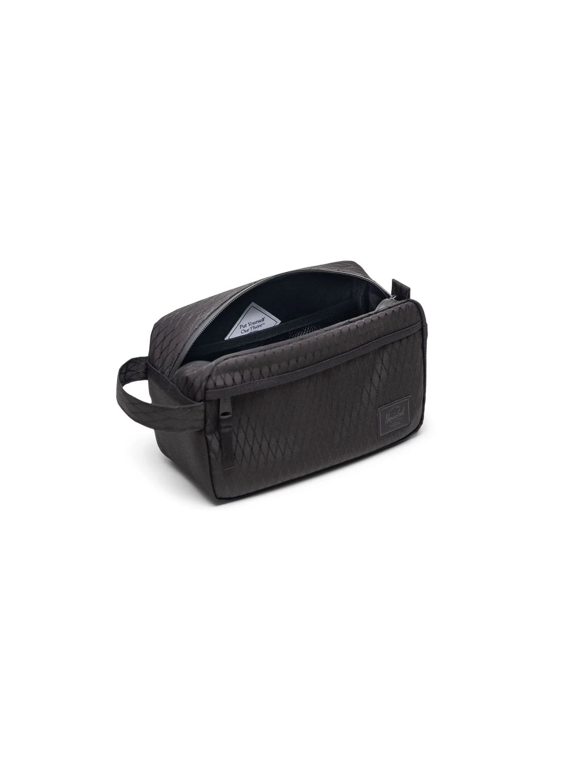 The Herschel Chapter Travel Kit - 5L is a black toiletry bag made from recycled polyester with a textured finish, side handle, zippered main compartment, grey interior, and small inner pocket. Shown open against a white background.